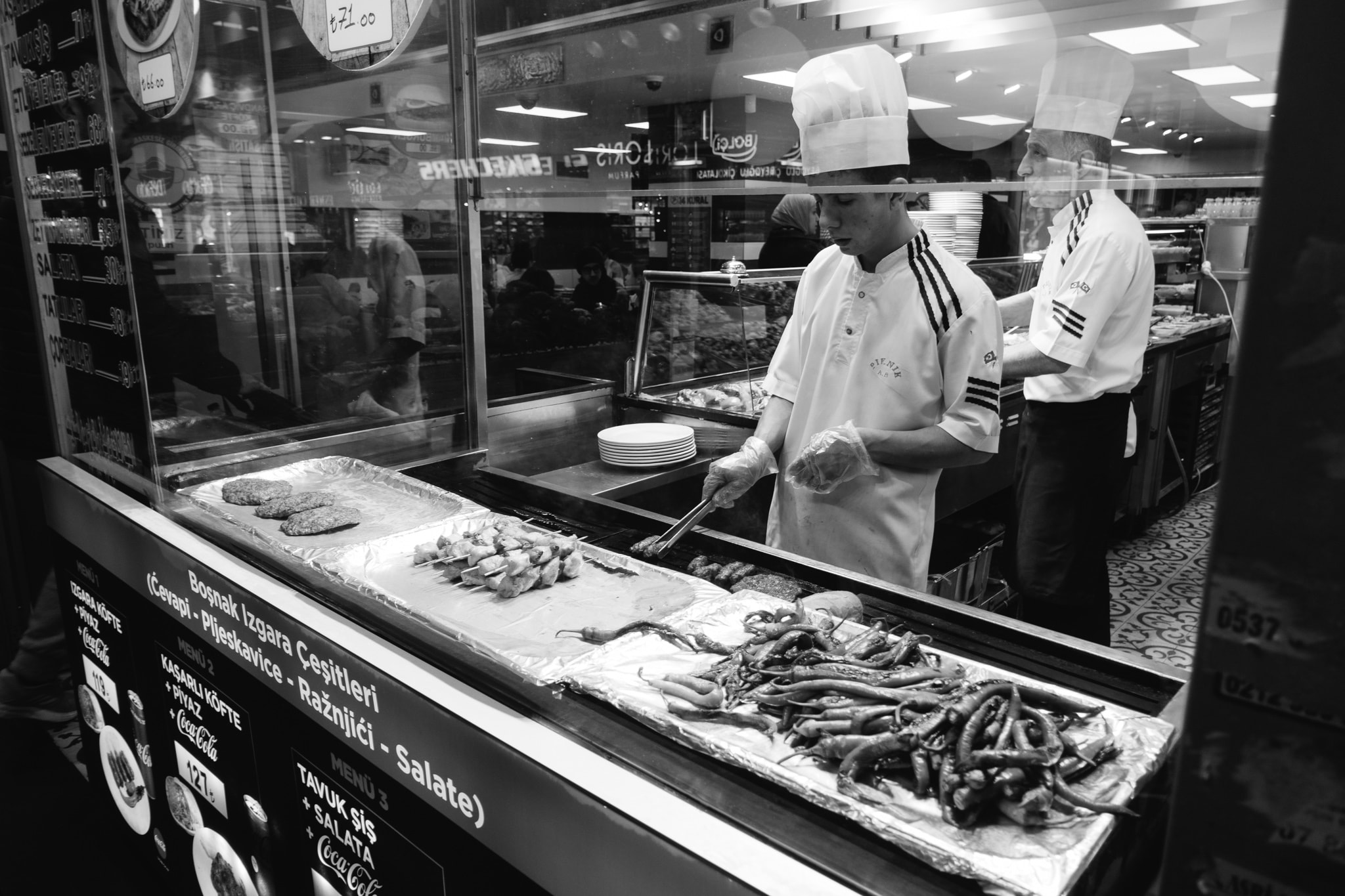 Two chefs preparing grilled meats and peppers at a Turkish restaurant counter