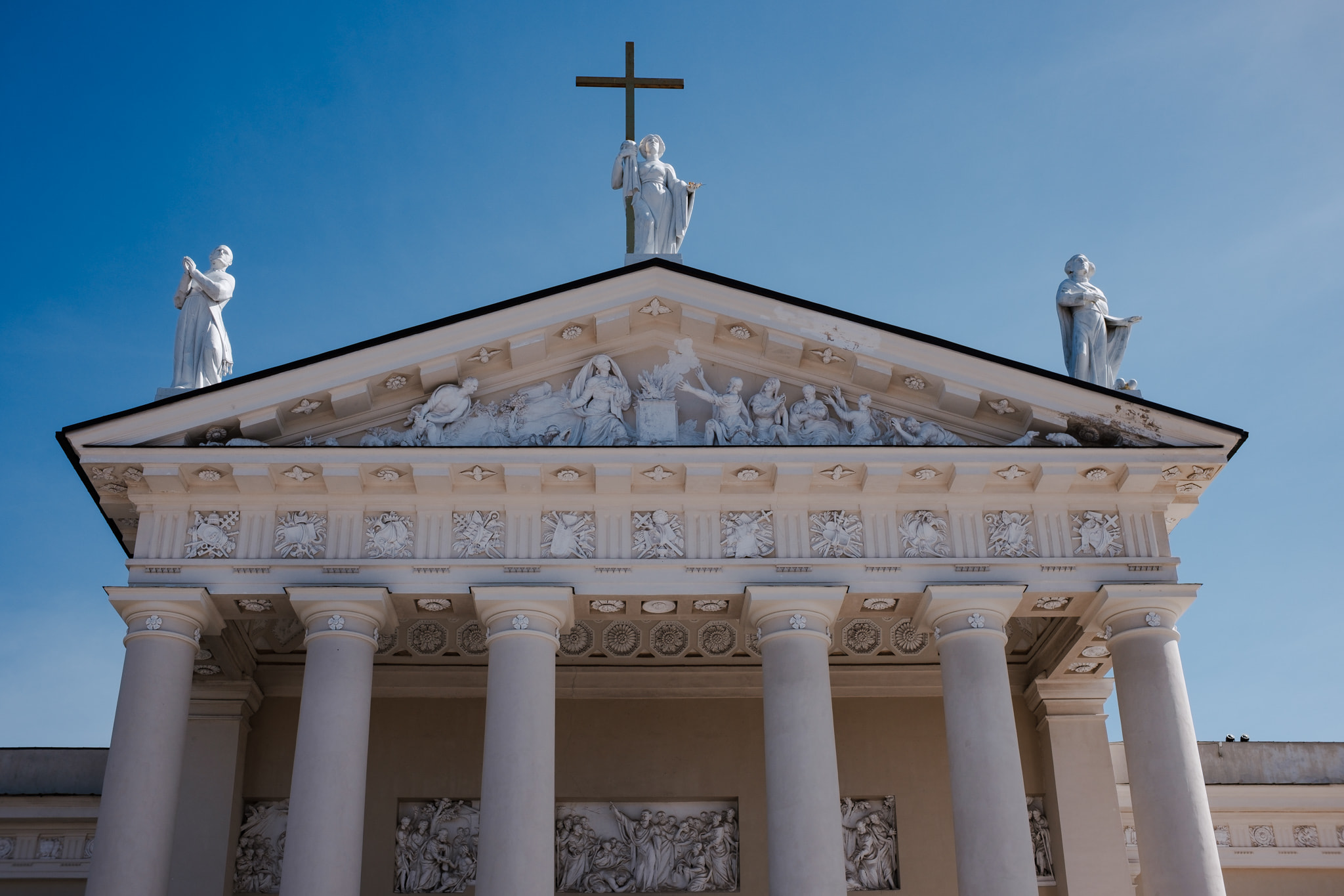 Classical church facade with statues and cross against blue sky