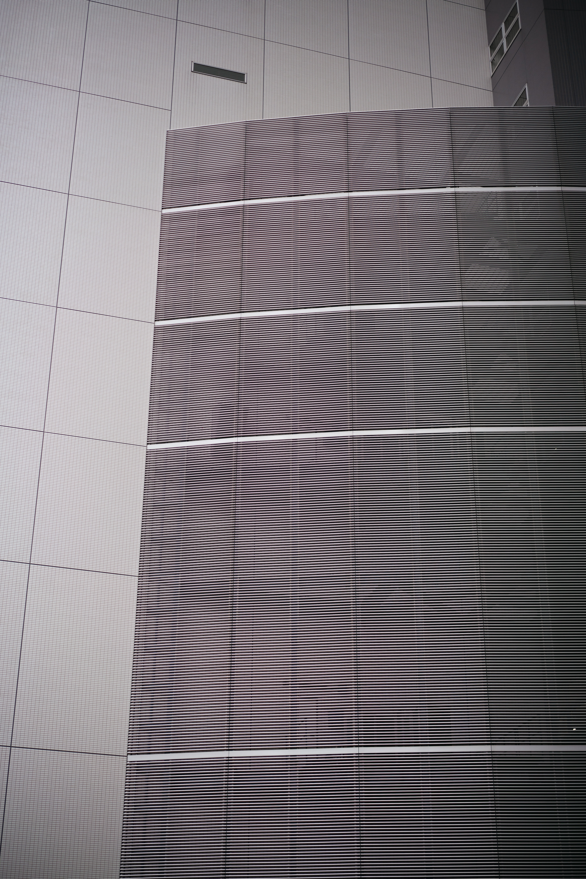 Modern building facade with curved slatted section and tiled wall