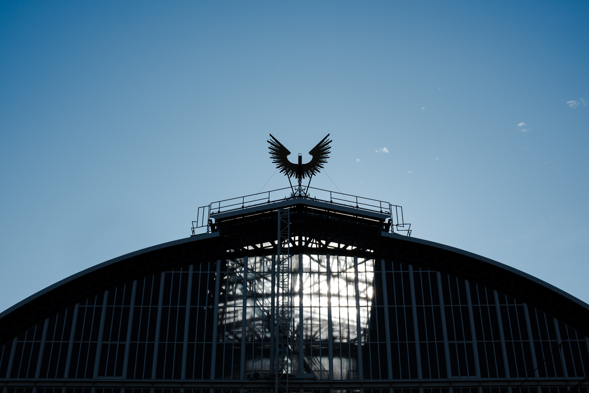 Eagle statue atop arched glass building against clear blue sky