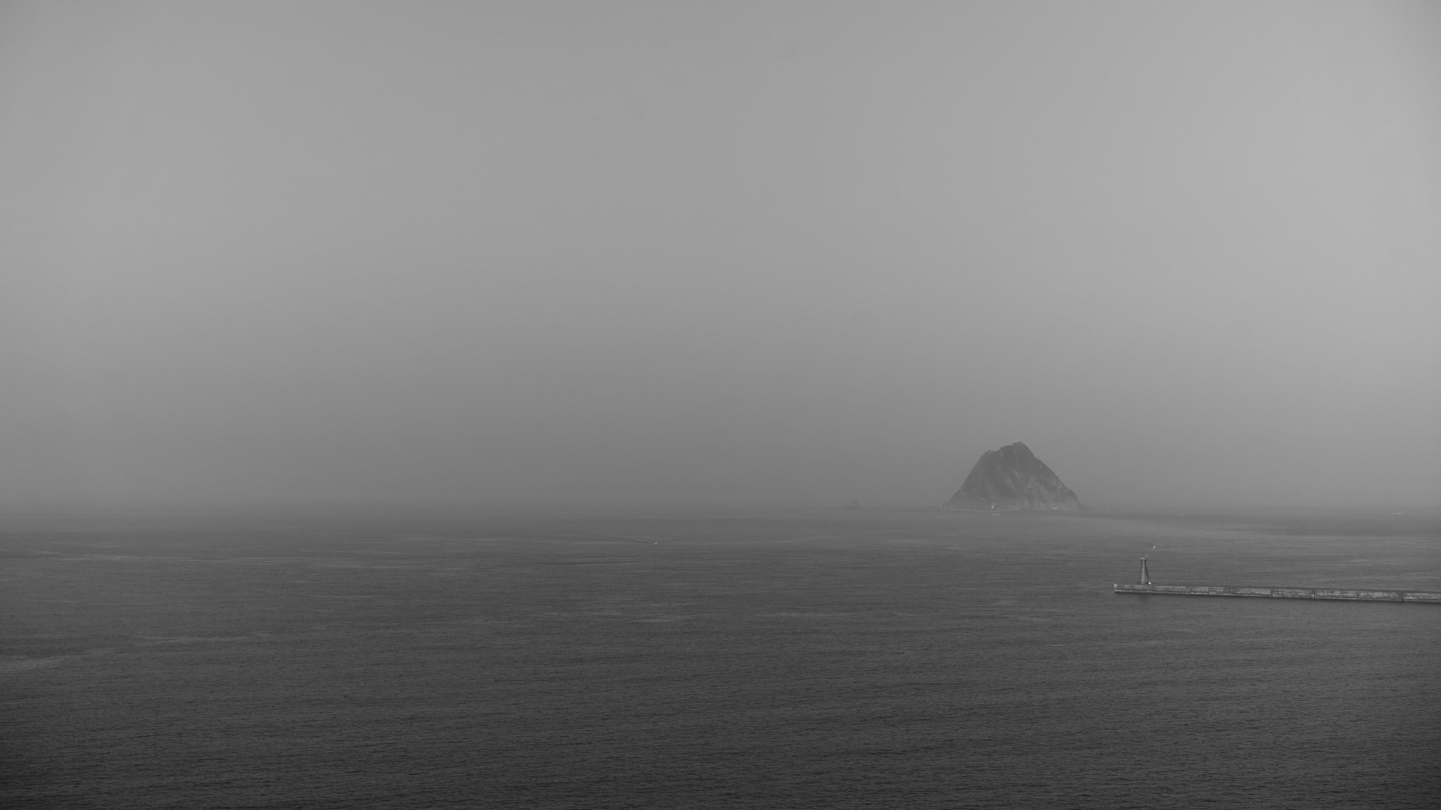 Misty coastal seascape with distant rocky island and pier