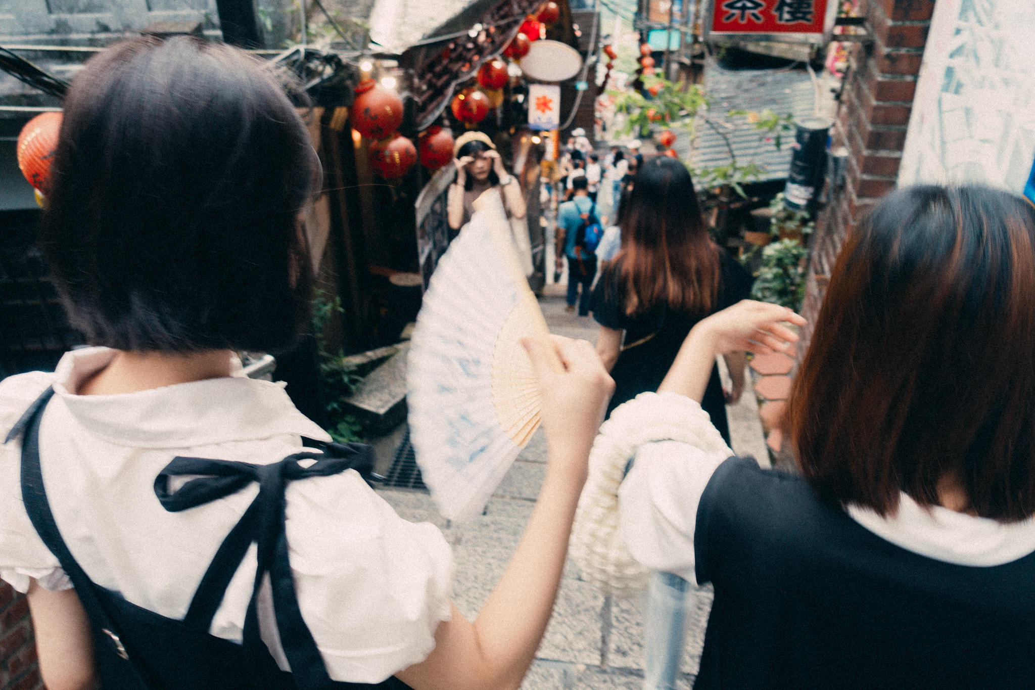 Women with paper fan walking down crowded alley in Jiufen Taiwan