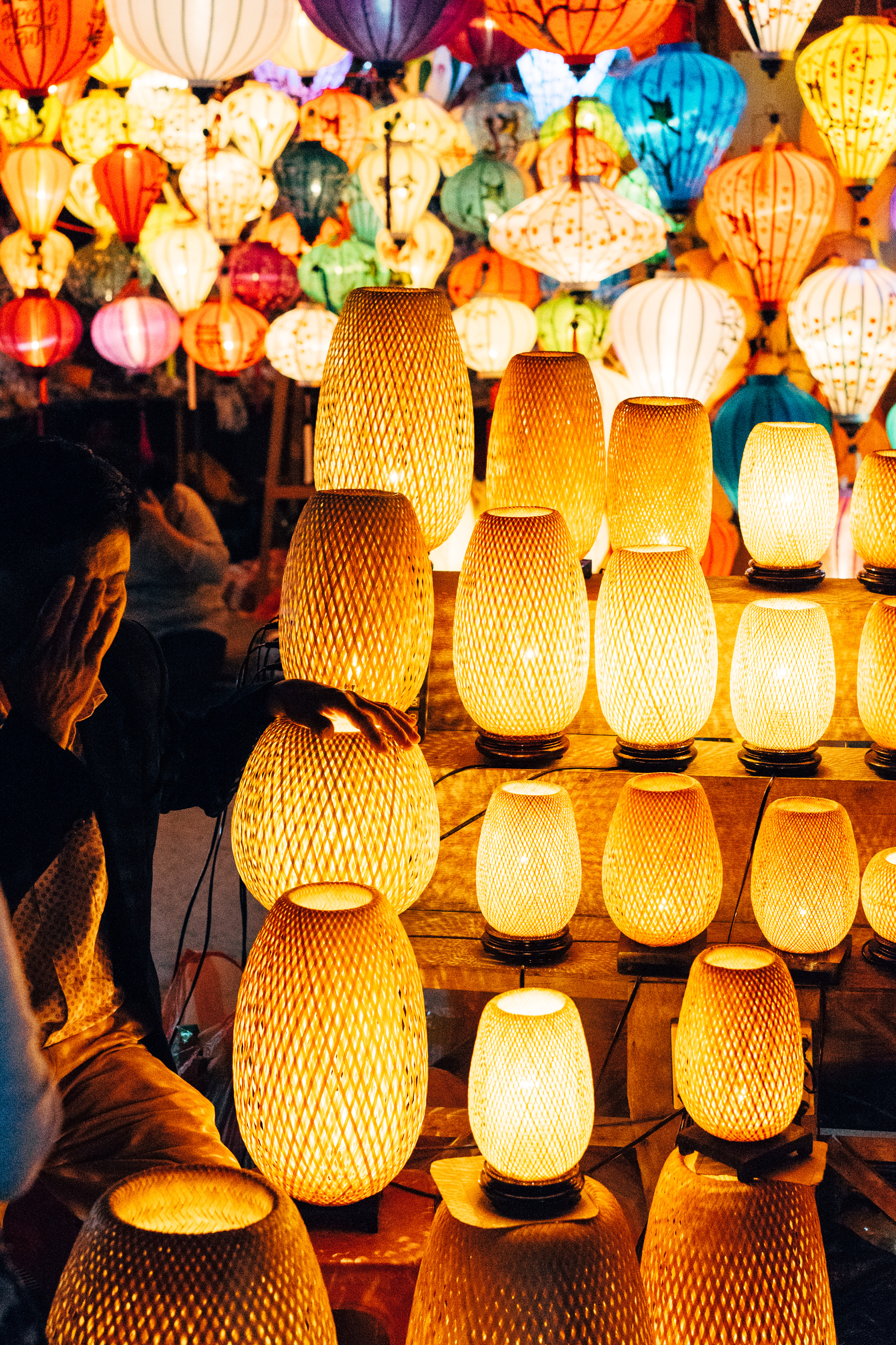 Vendor arranging glowing woven lanterns at a bustling night market