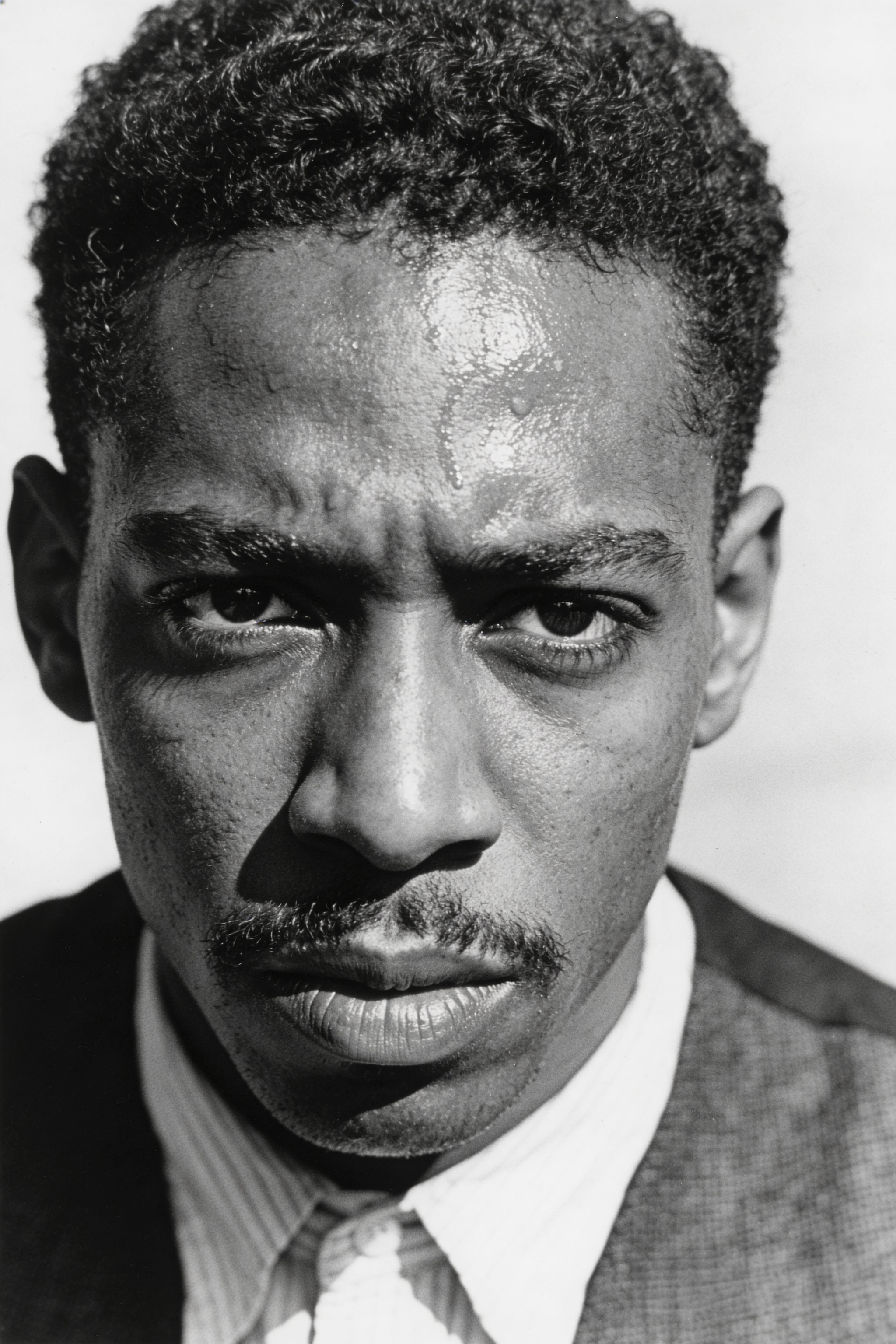 Close-up black and white portrait of a man with intense expression and glistening skin.