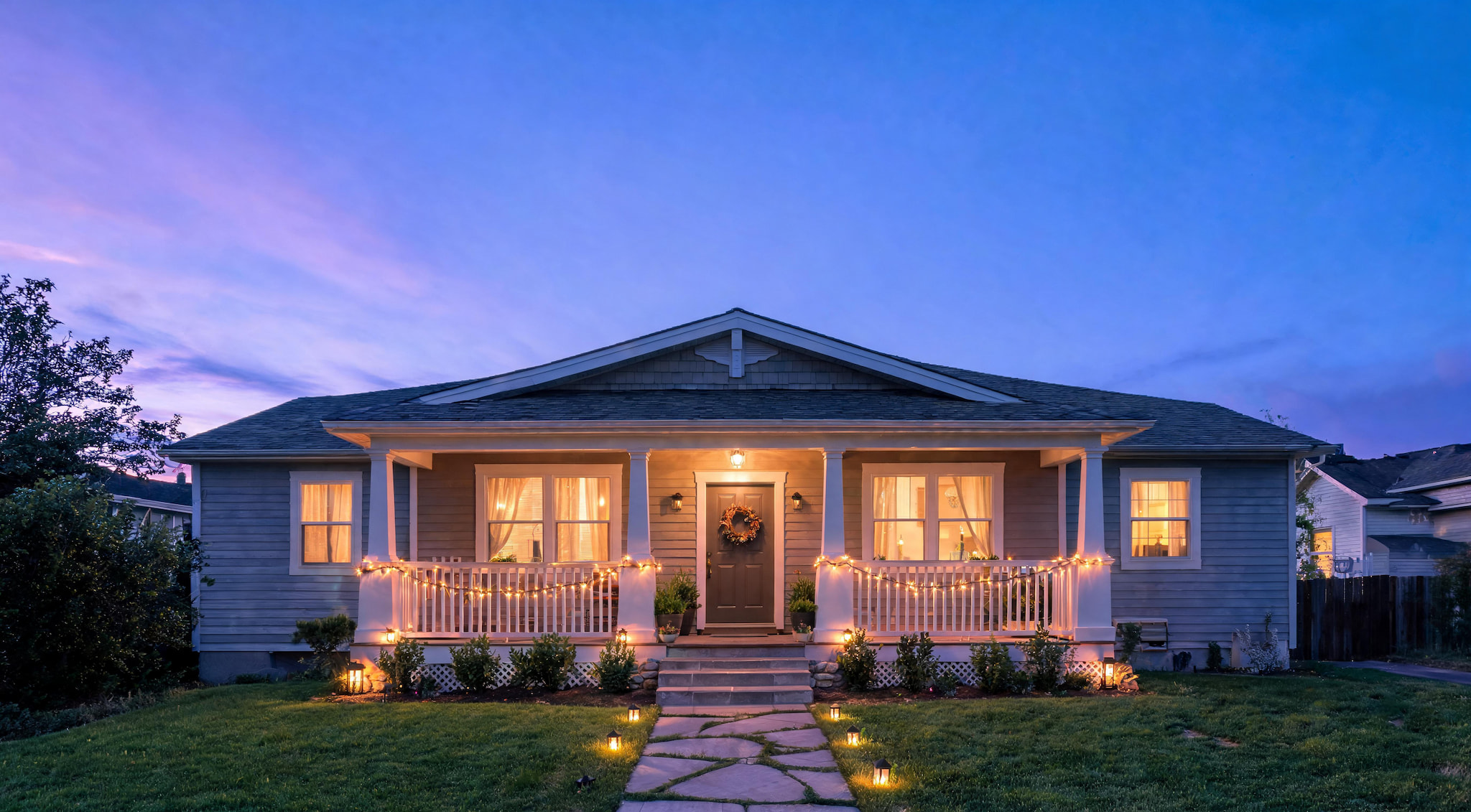 Modern ranch-style home at twilight with lit windows and decorative string lights on the porch