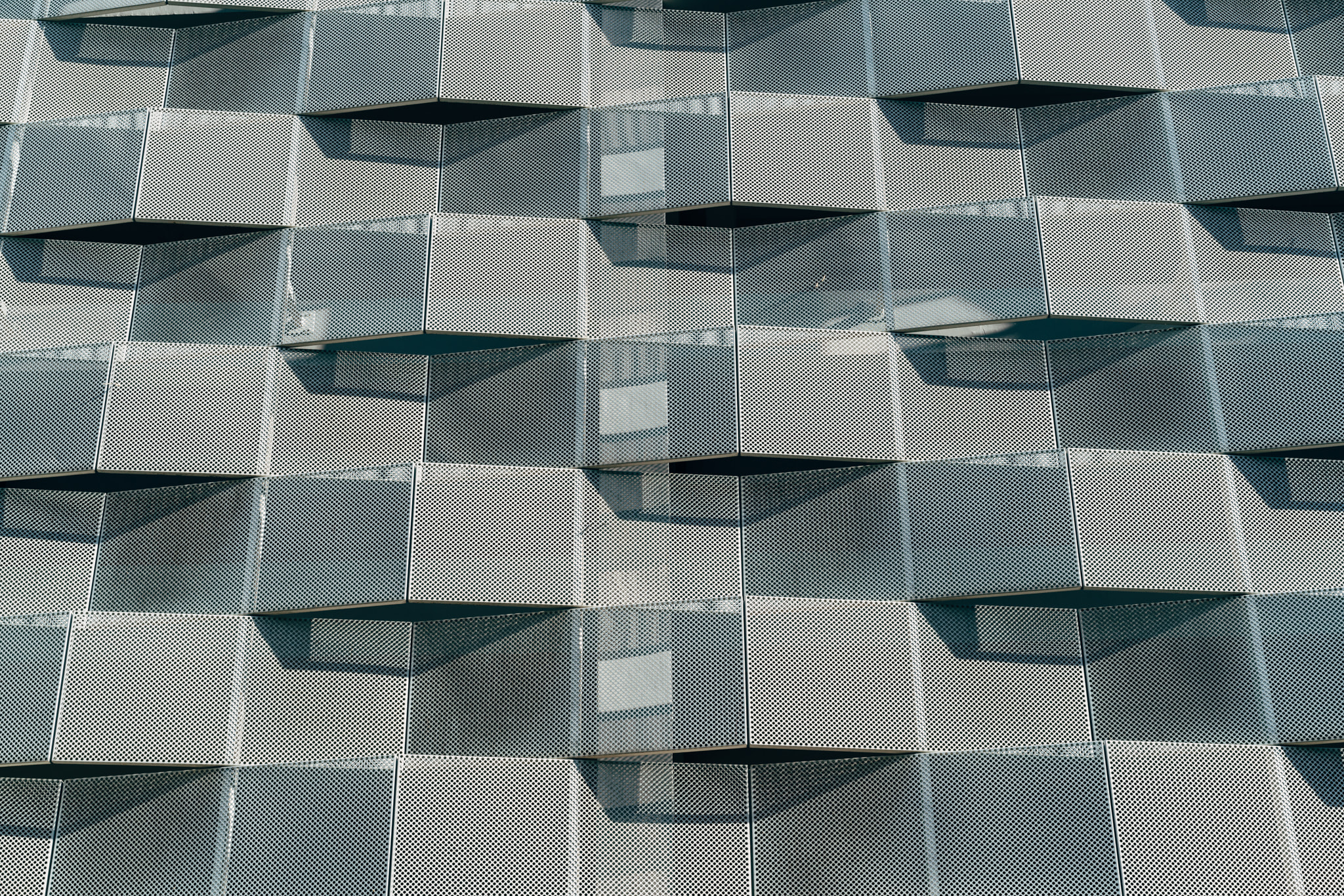 Modern perforated metal facade with geometric 3D pattern and shadows