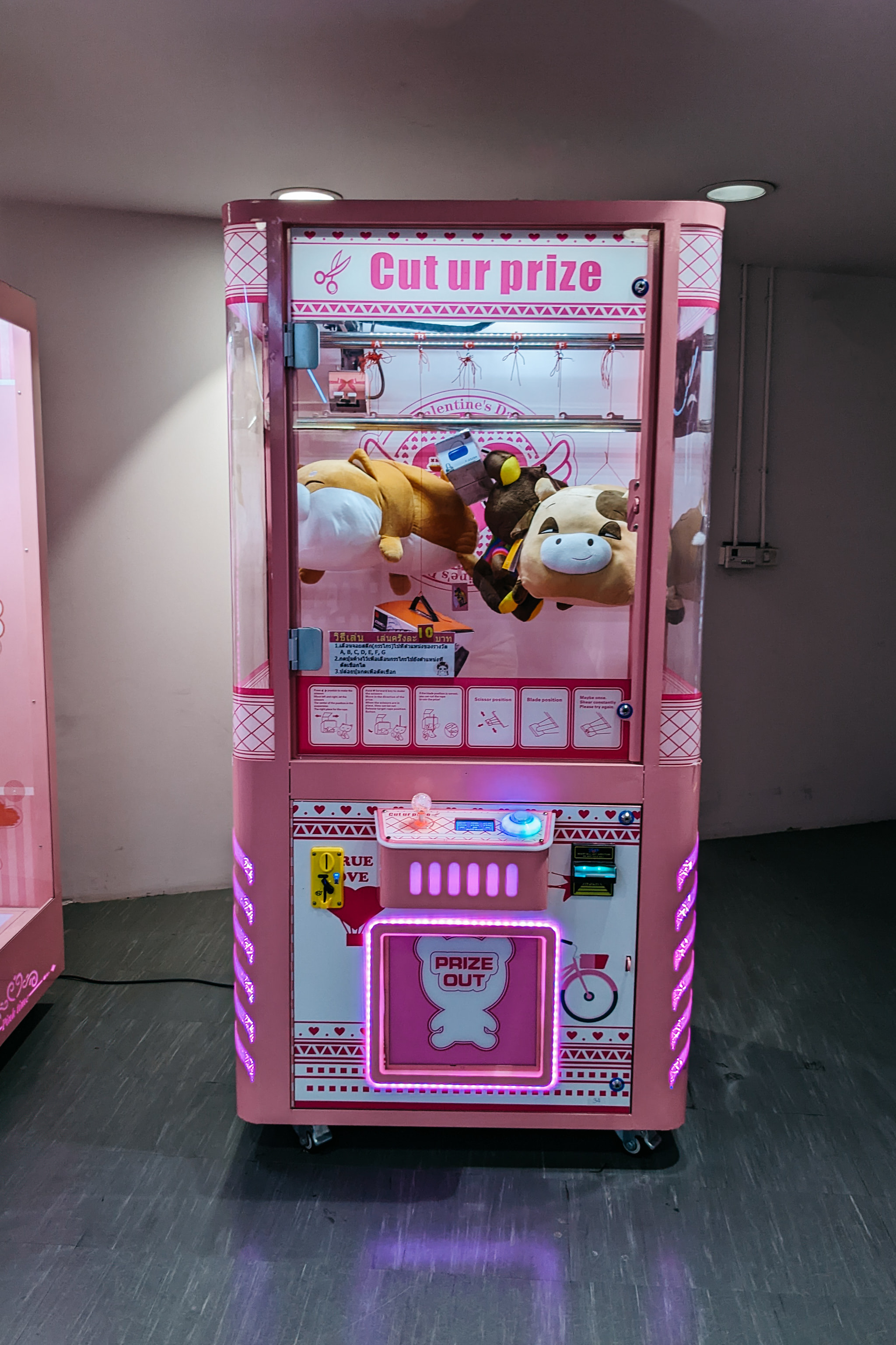 Pink claw machine with plush toys inside an arcade