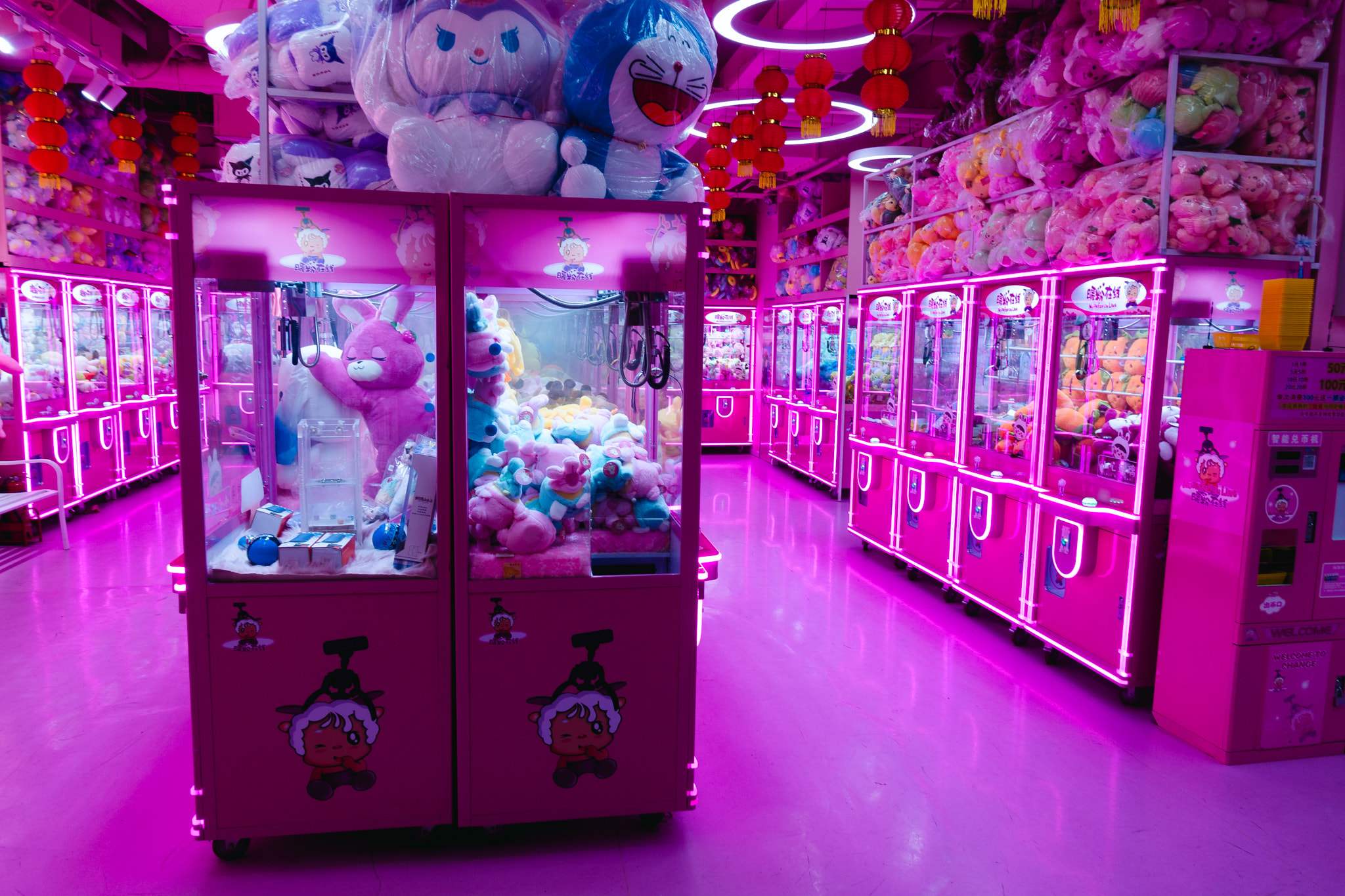 Pink claw machine arcade filled with stuffed animals and toys under vibrant neon lighting