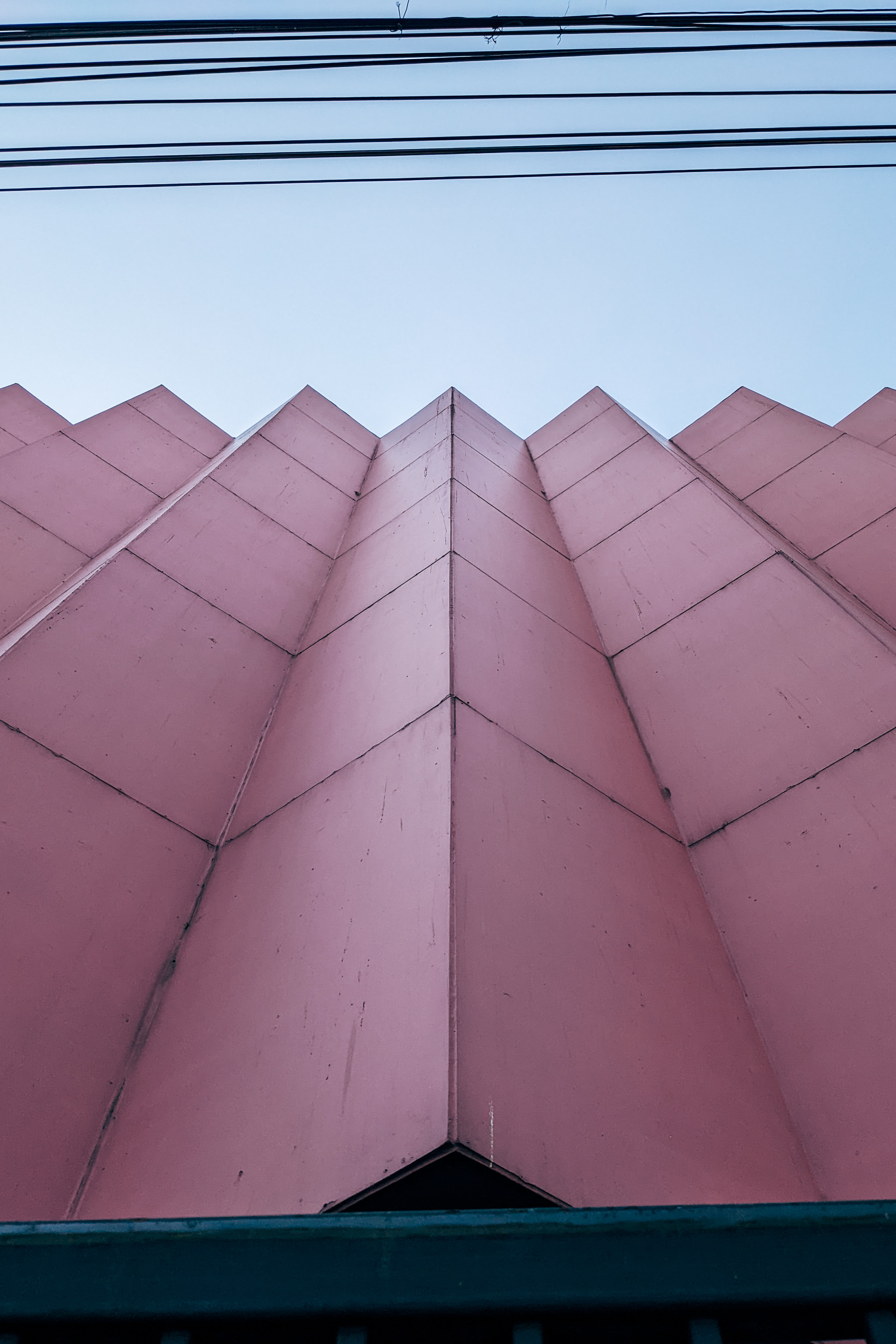 Low angle view of pink geometric building facade with power lines against pale sky