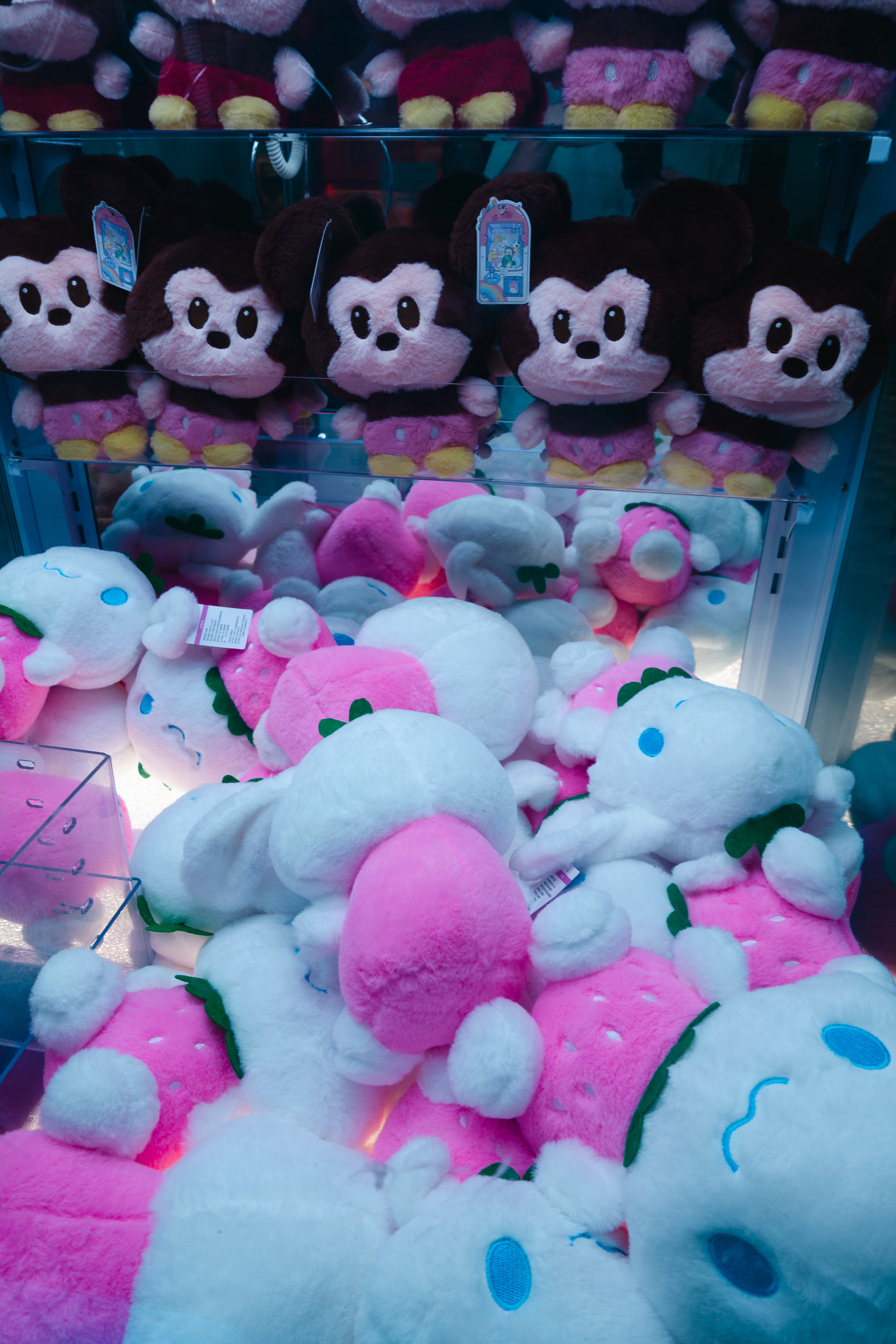 A claw machine filled with plush toys including Mickey Mouse and strawberry-themed characters.