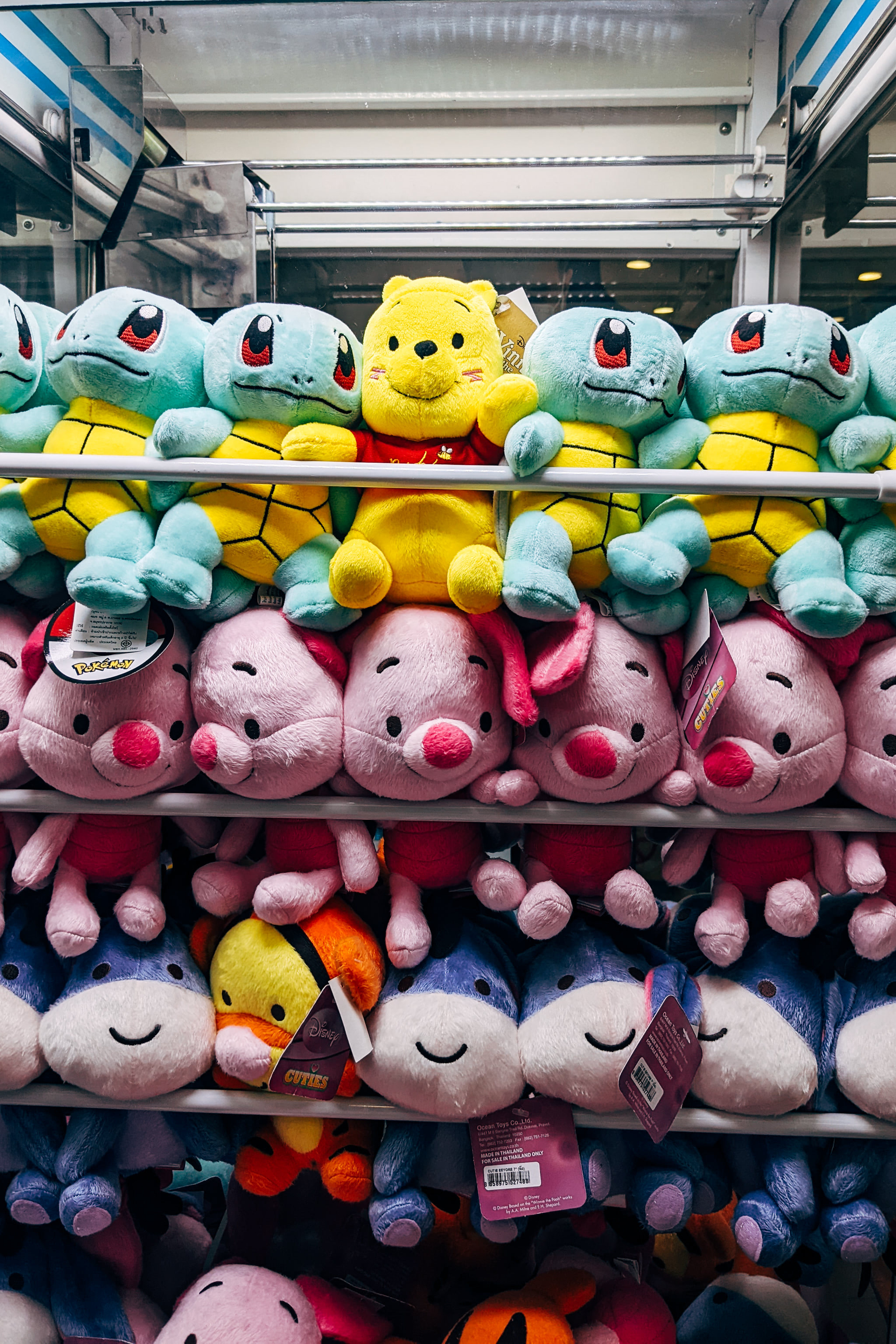 Rows of plush toys featuring cartoon characters like yellow bears, turtles, and pink pigs inside a prize machine.