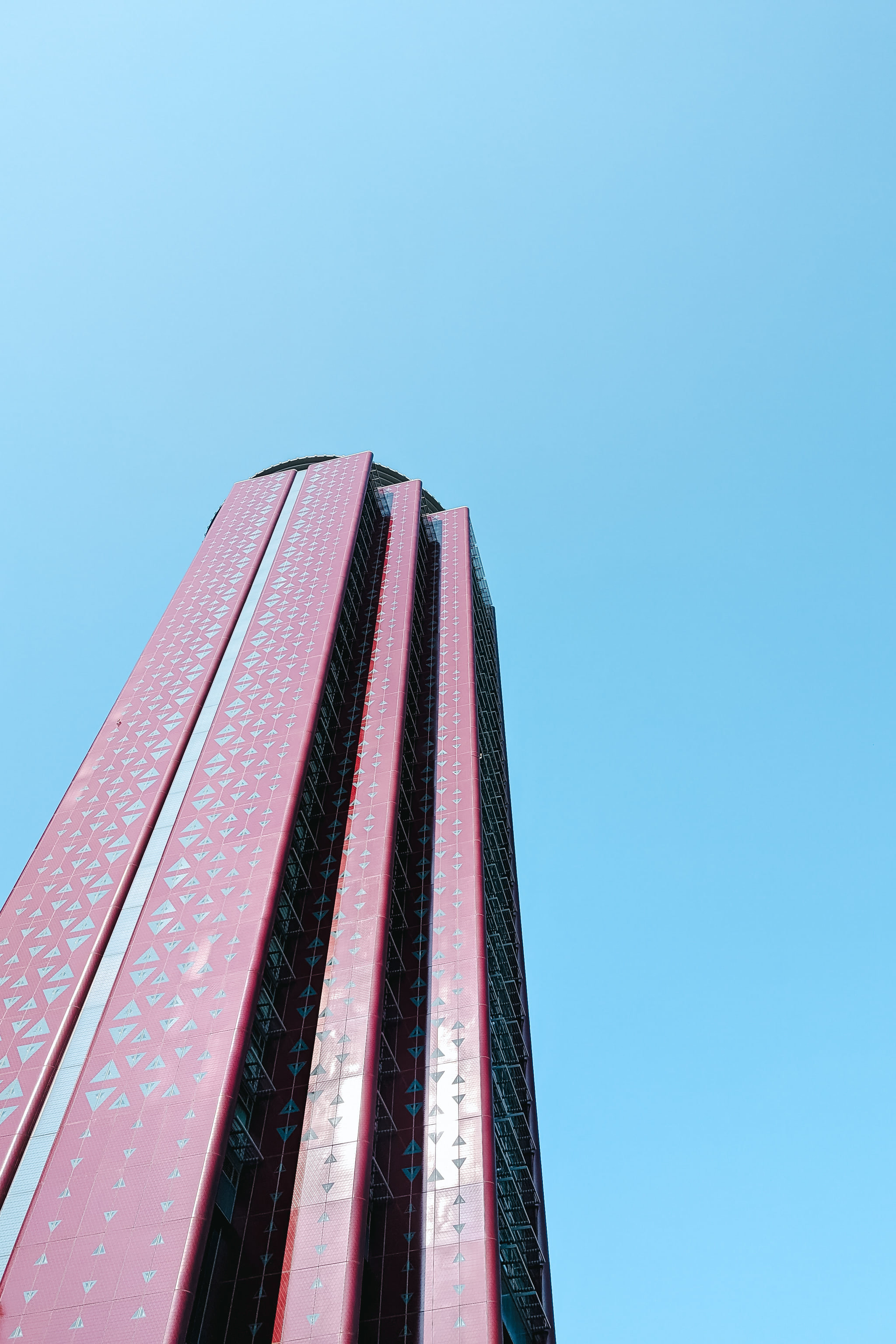 Low-angle view of a modern red skyscraper against a clear blue sky