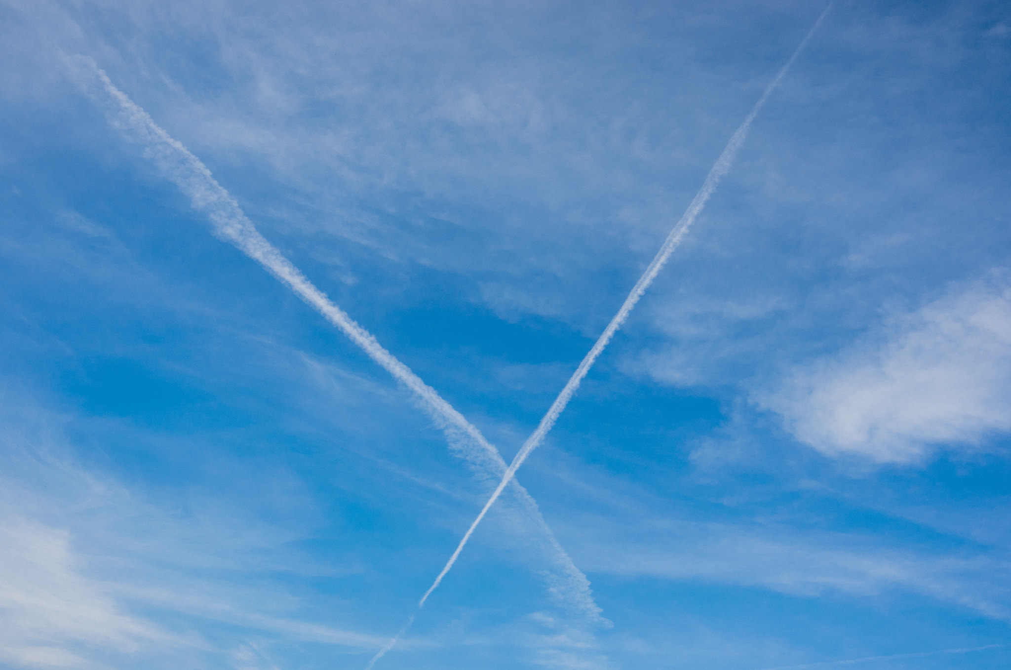 Blue sky with intersecting white contrails from aircraft