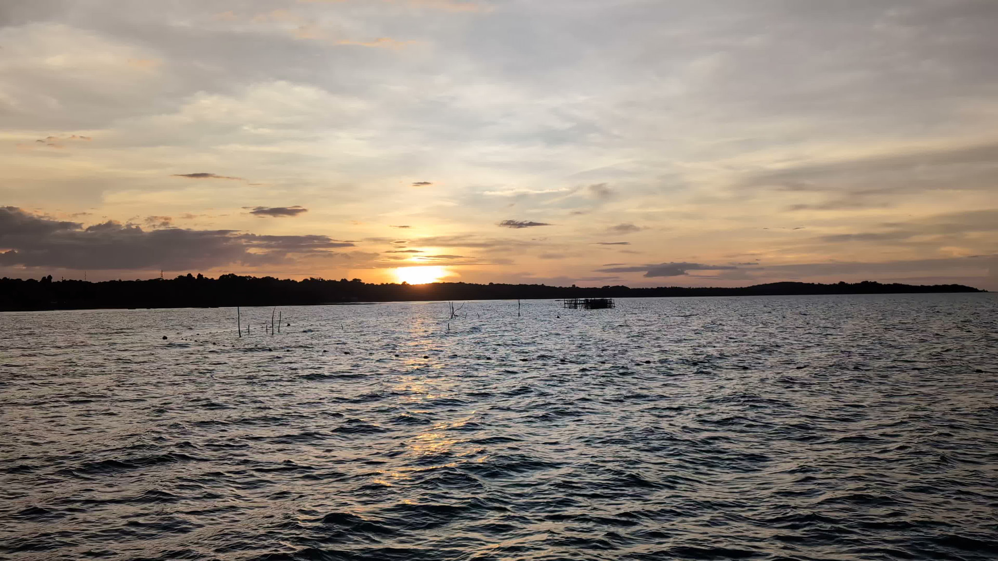 Sunset over a calm sea with distant shoreline and wooden posts in water