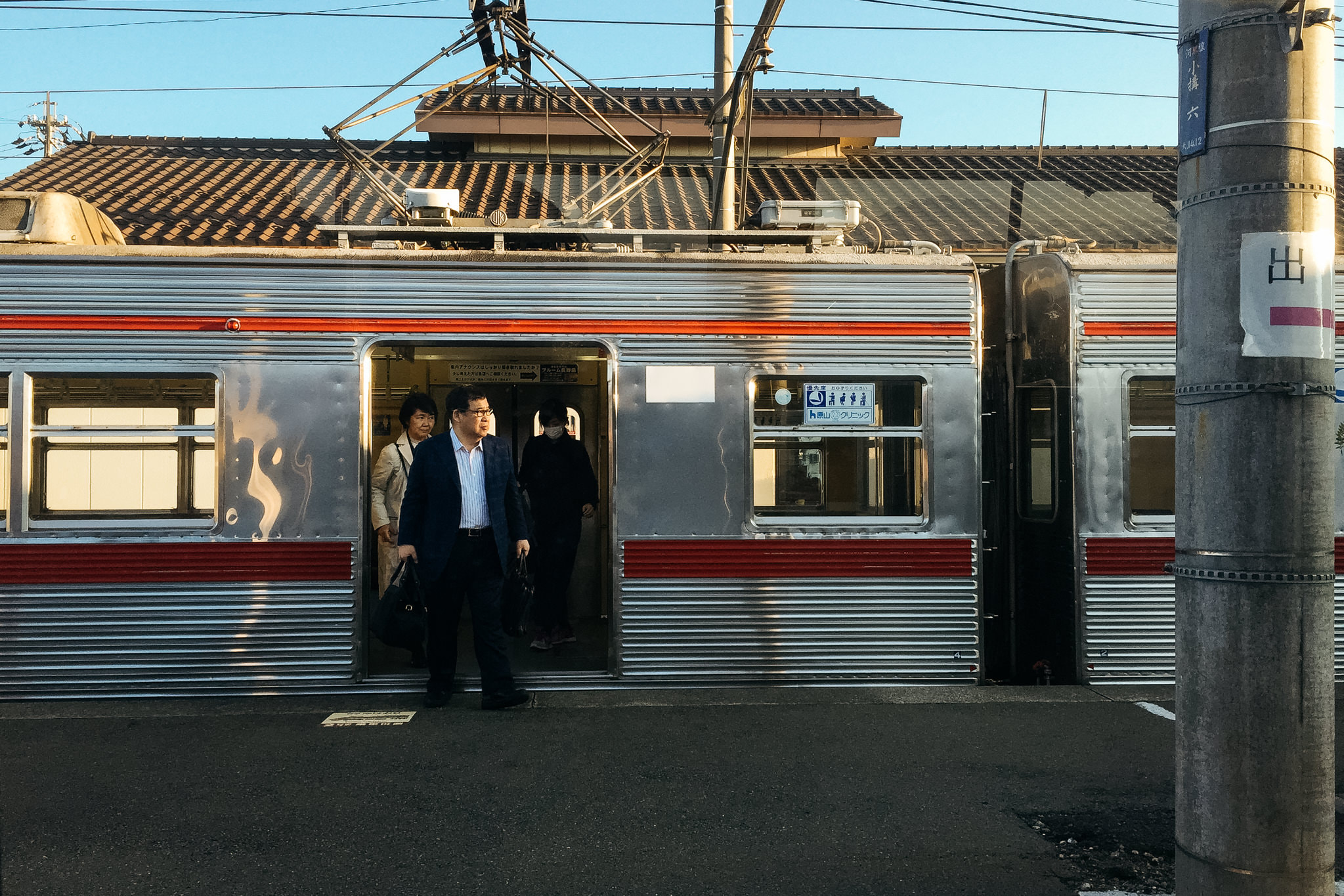 Commuters disembarking from a silver and red train at a Japanese railway station platform