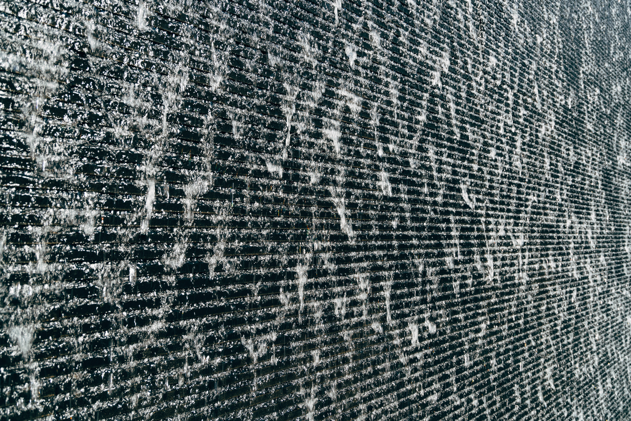 Close-up of water cascading over dark horizontal slats in a modern water wall fountain