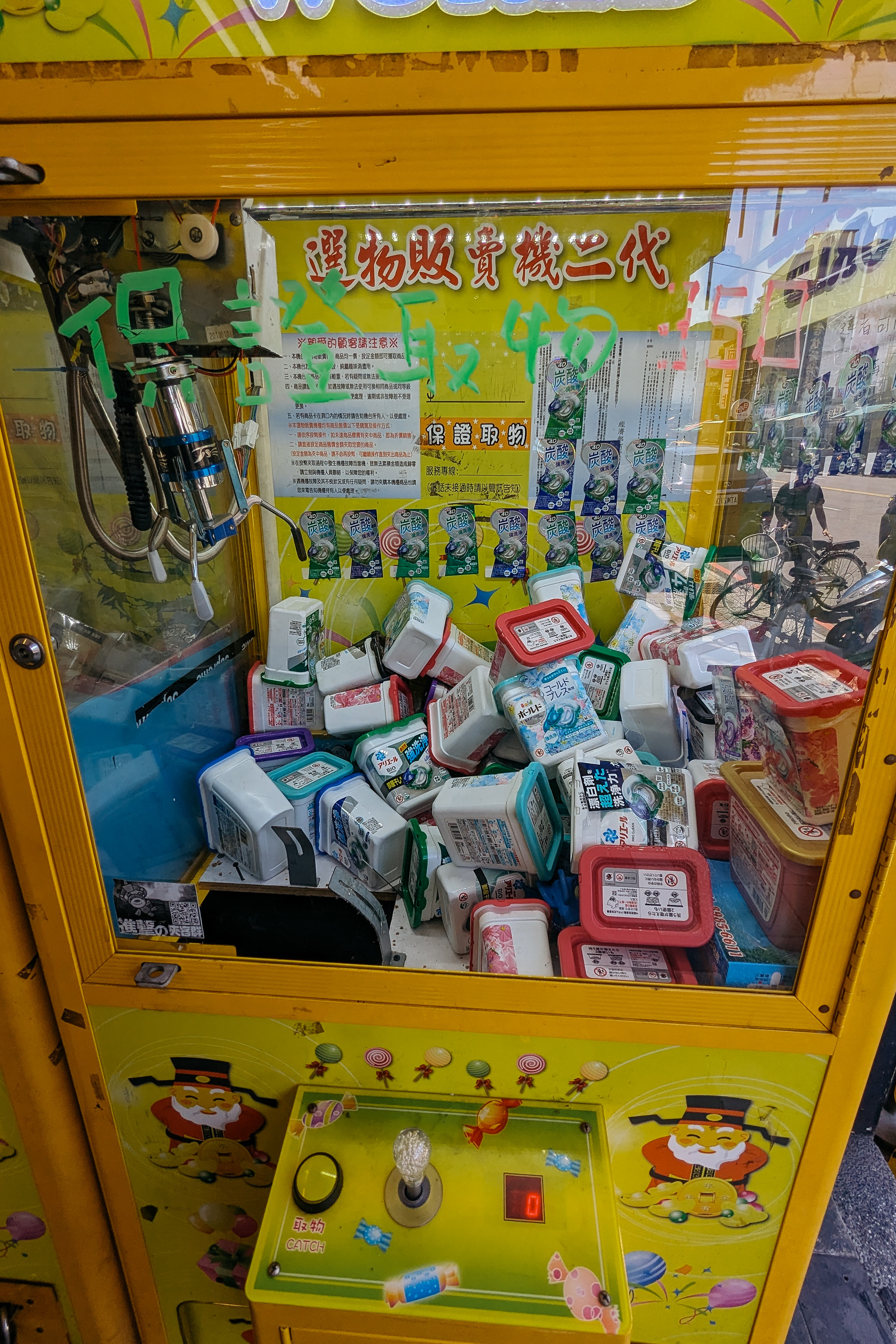 Yellow claw machine filled with plastic containers and prizes at an outdoor street arcade