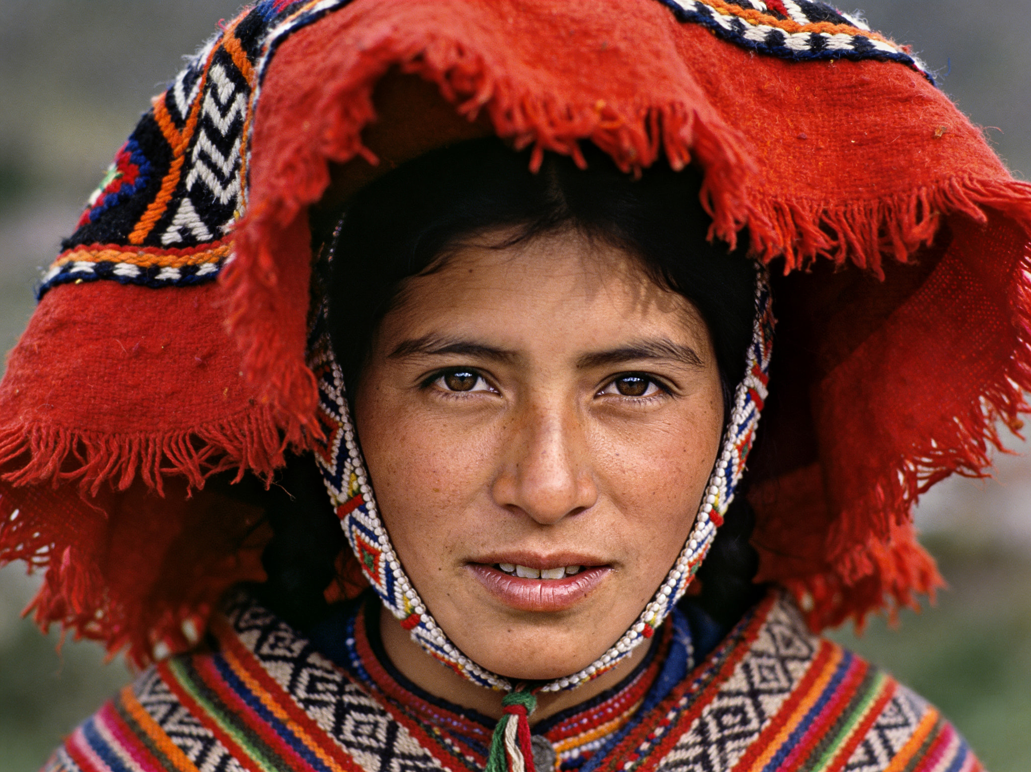 Portrait of a woman wearing traditional Andean red headgear and woven textiles