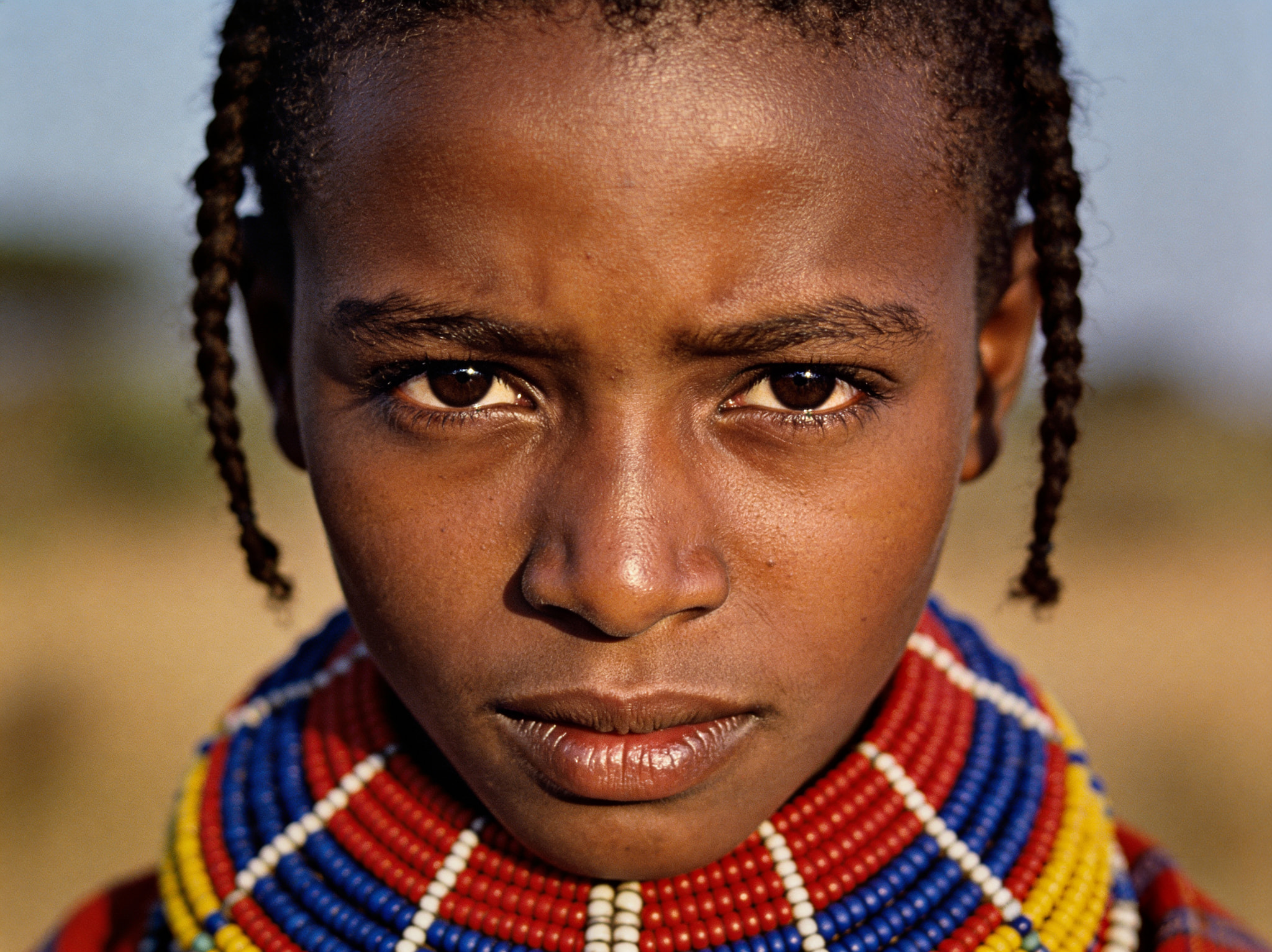 Close-up portrait of a young girl with braided hair wearing a vibrant multi-colored beaded necklace.