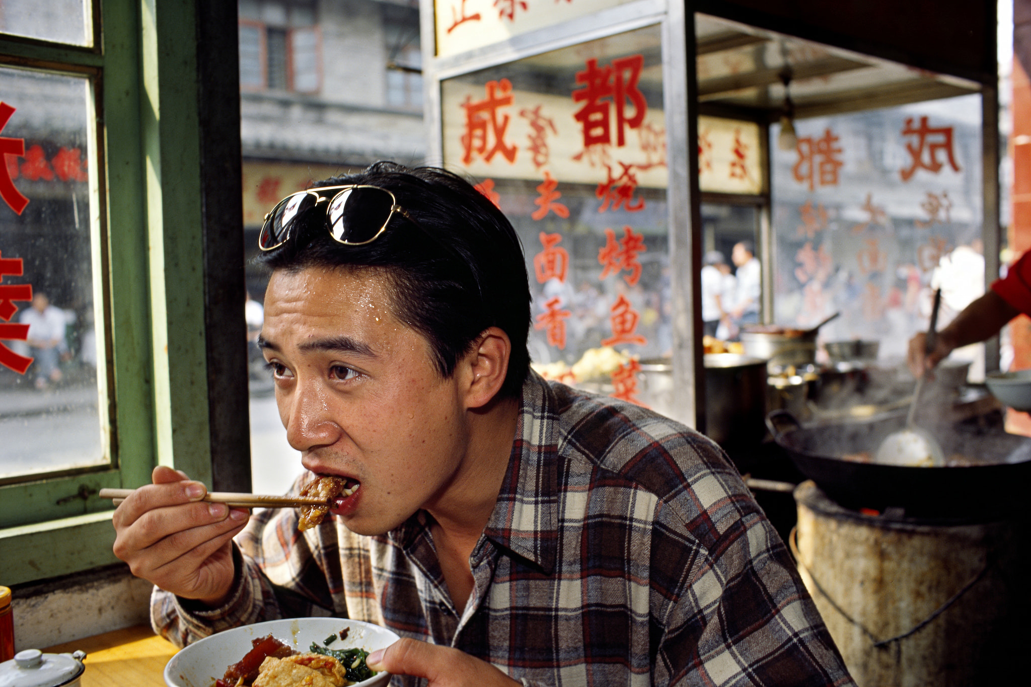 A man eating lunch with chopsticks at a busy roadside food stall in China.
