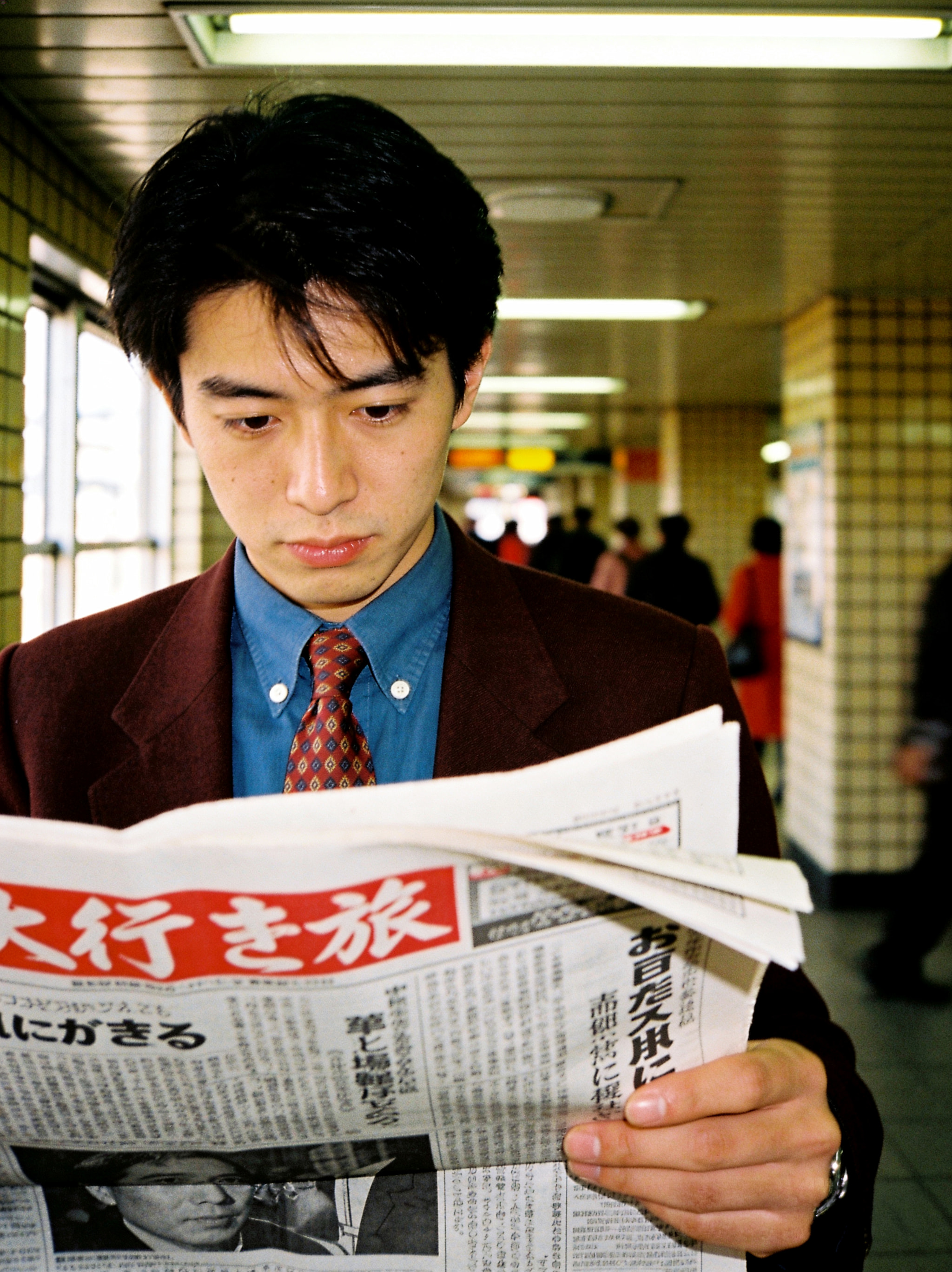 Young East Asian man in a suit reading a newspaper inside a subway station