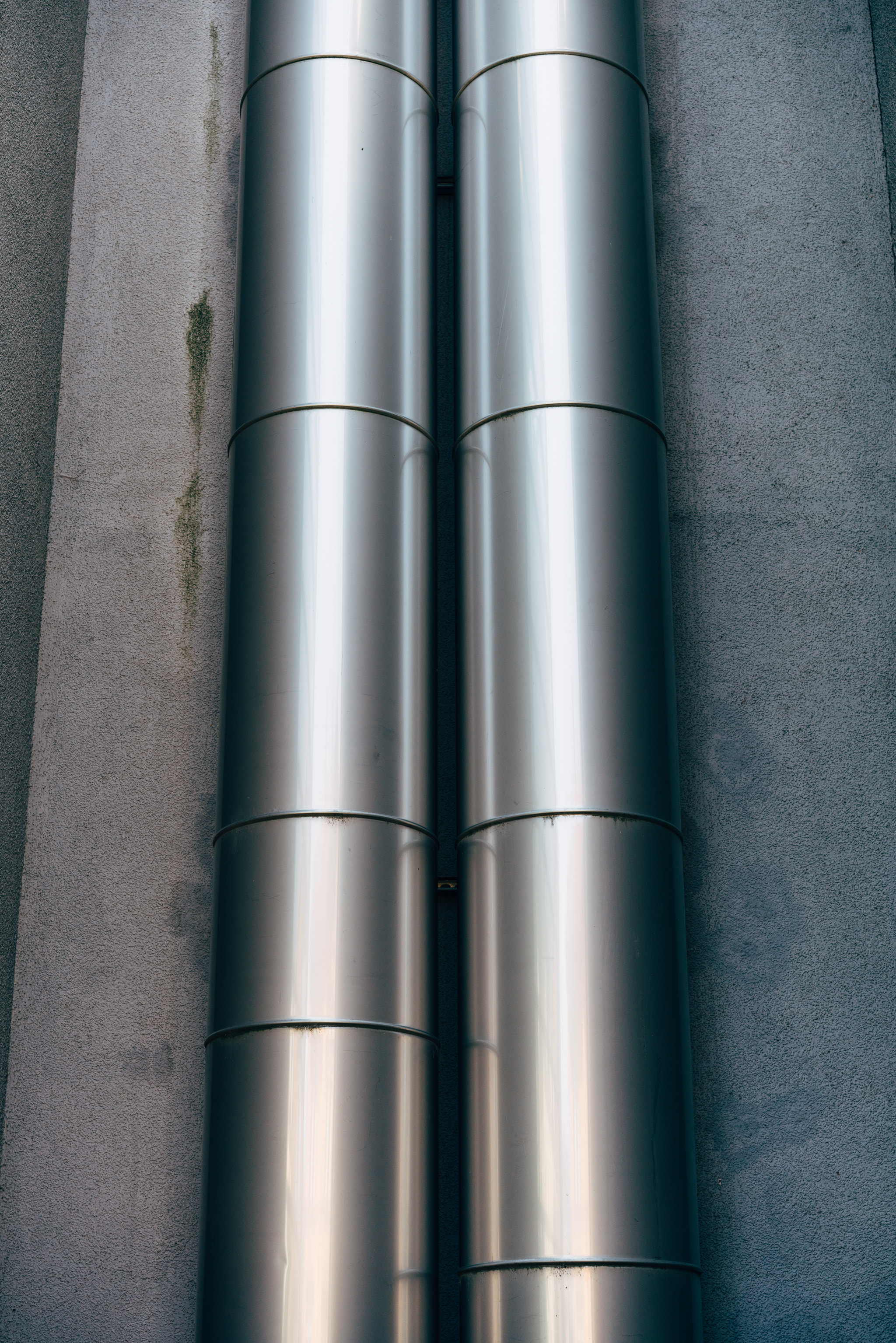 Two parallel metallic pipes mounted on a rough concrete wall.