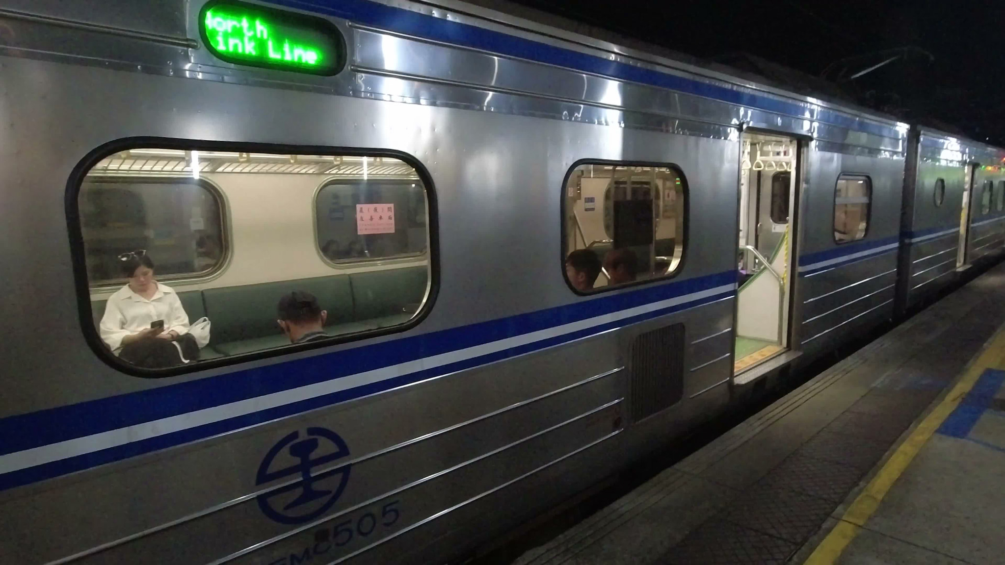 A passenger train stopped at a platform at night with passengers visible through the windows.