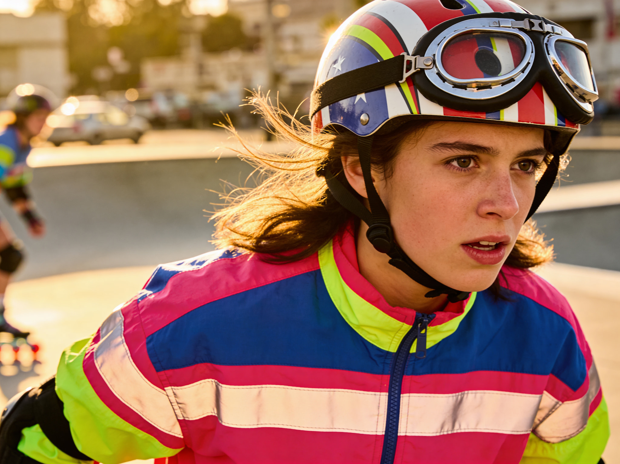 Young person wearing a colorful retro helmet and goggles roller skating at an outdoor park.