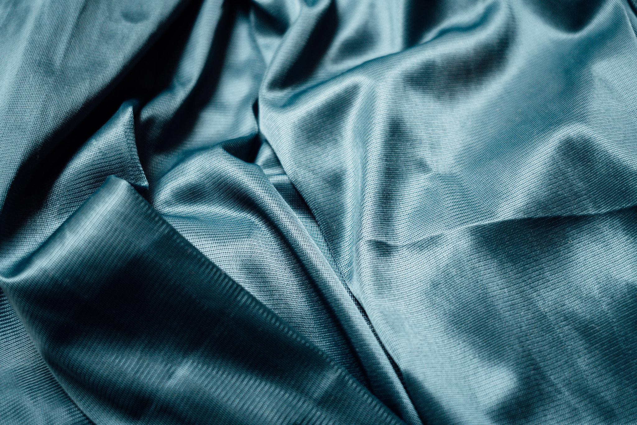 Close up of teal blue satin fabric with soft folds and shadows.
