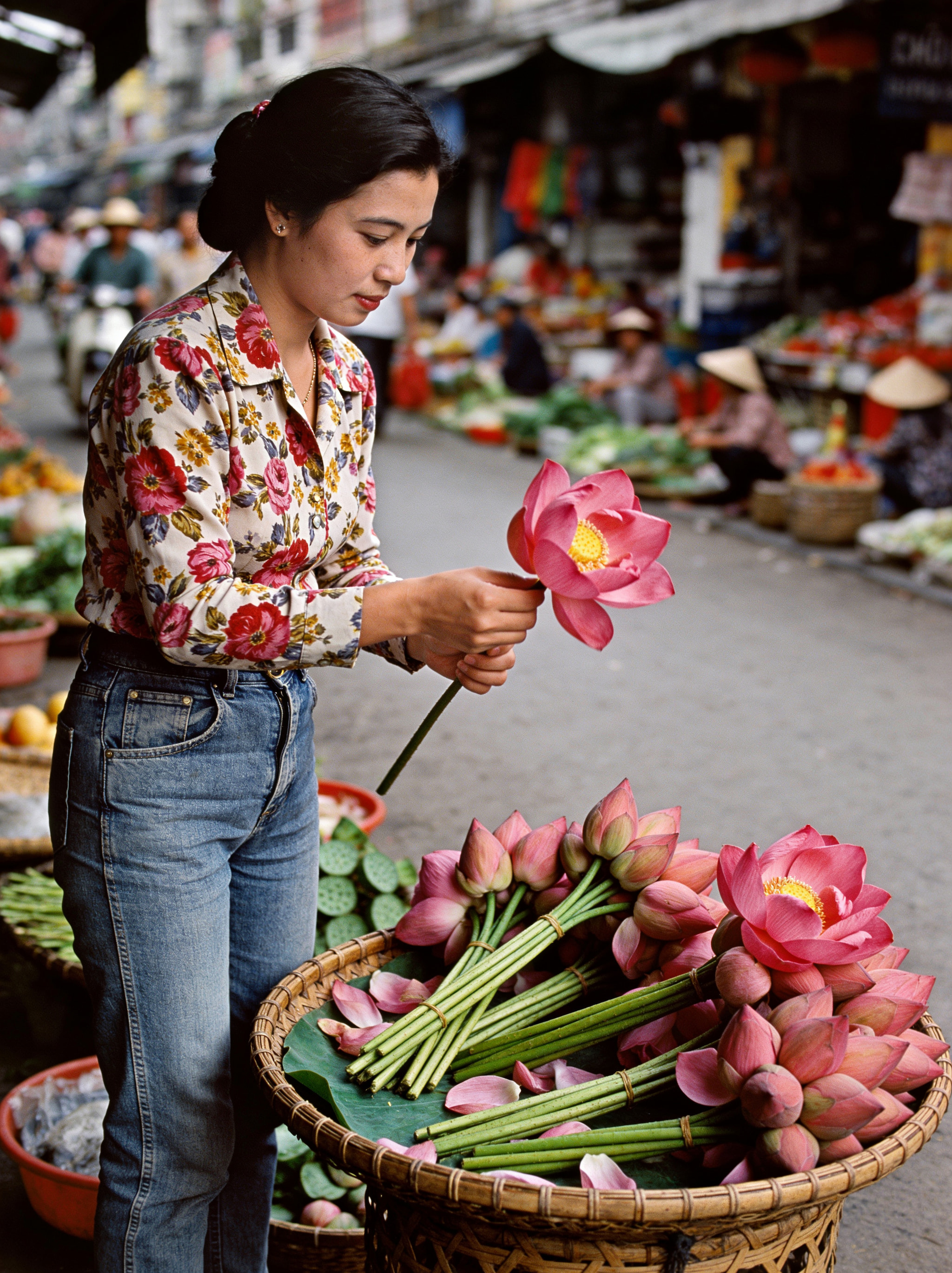 A woman holding a pink lotus flower at an outdoor street market.