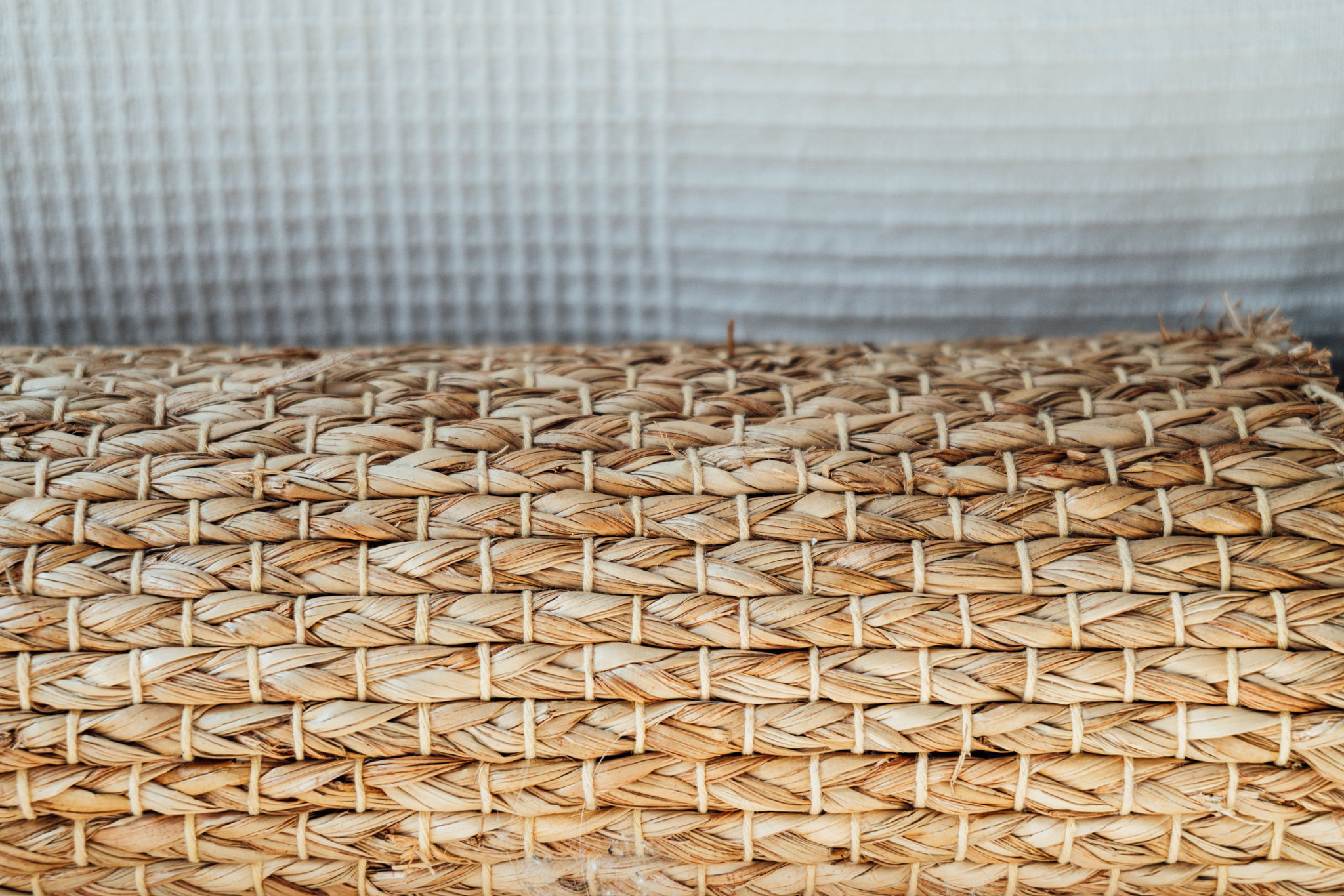 Close-up of a woven seagrass or jute rug roll texture against a white linen background
