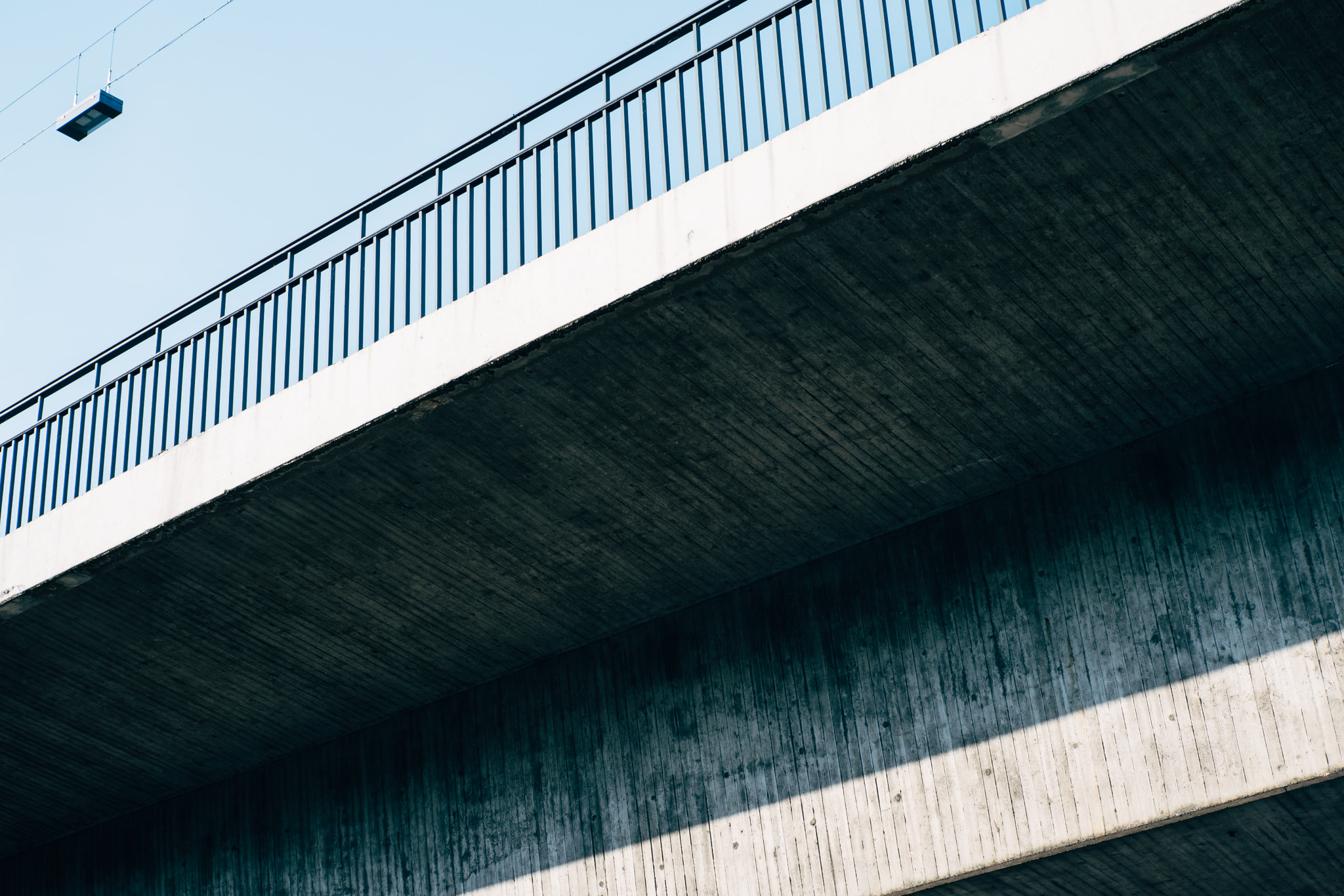 Underside of a modern concrete overpass bridge against a clear blue sky
