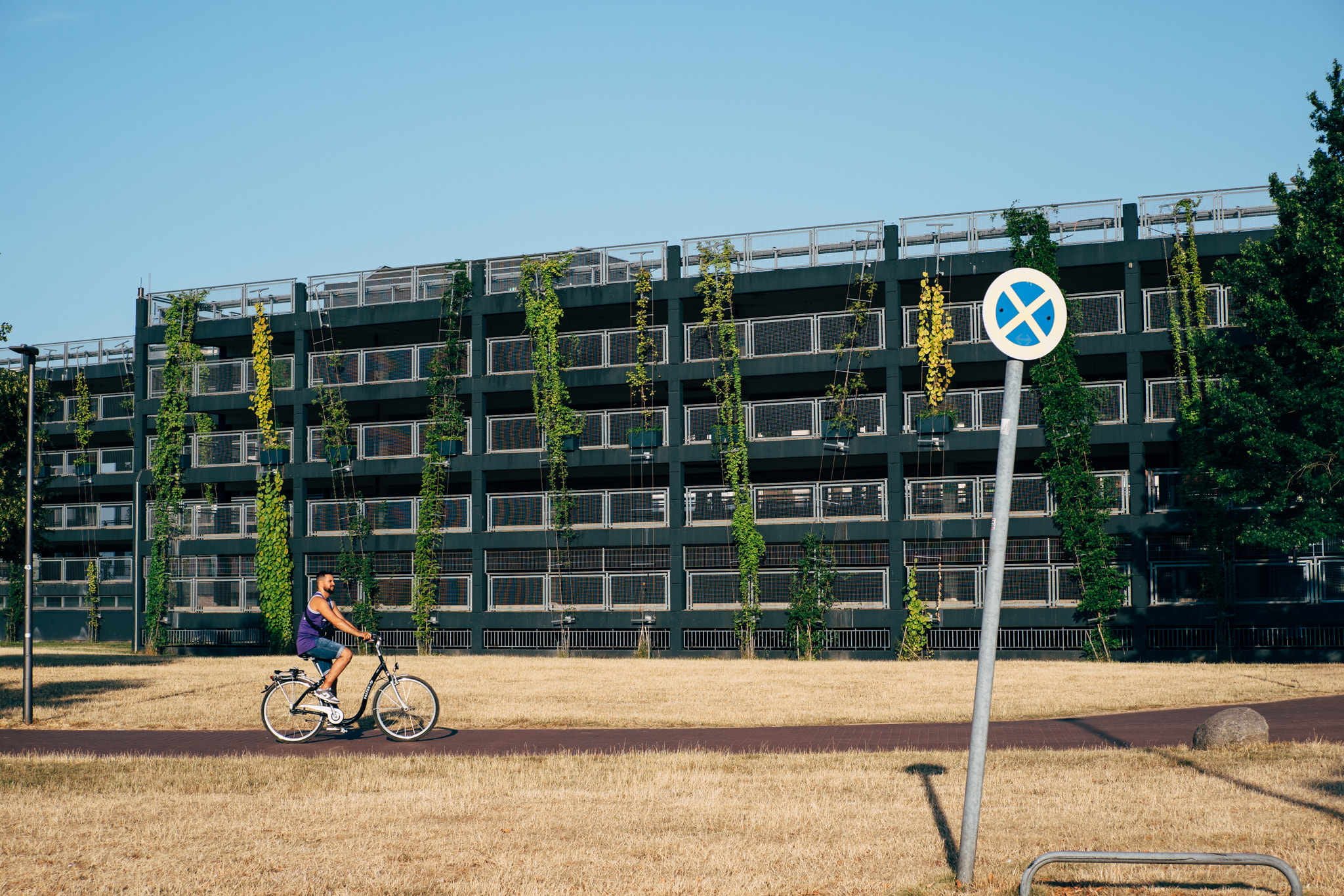 A man riding a bicycle on a path in front of a modern parking garage with vertical gardens.