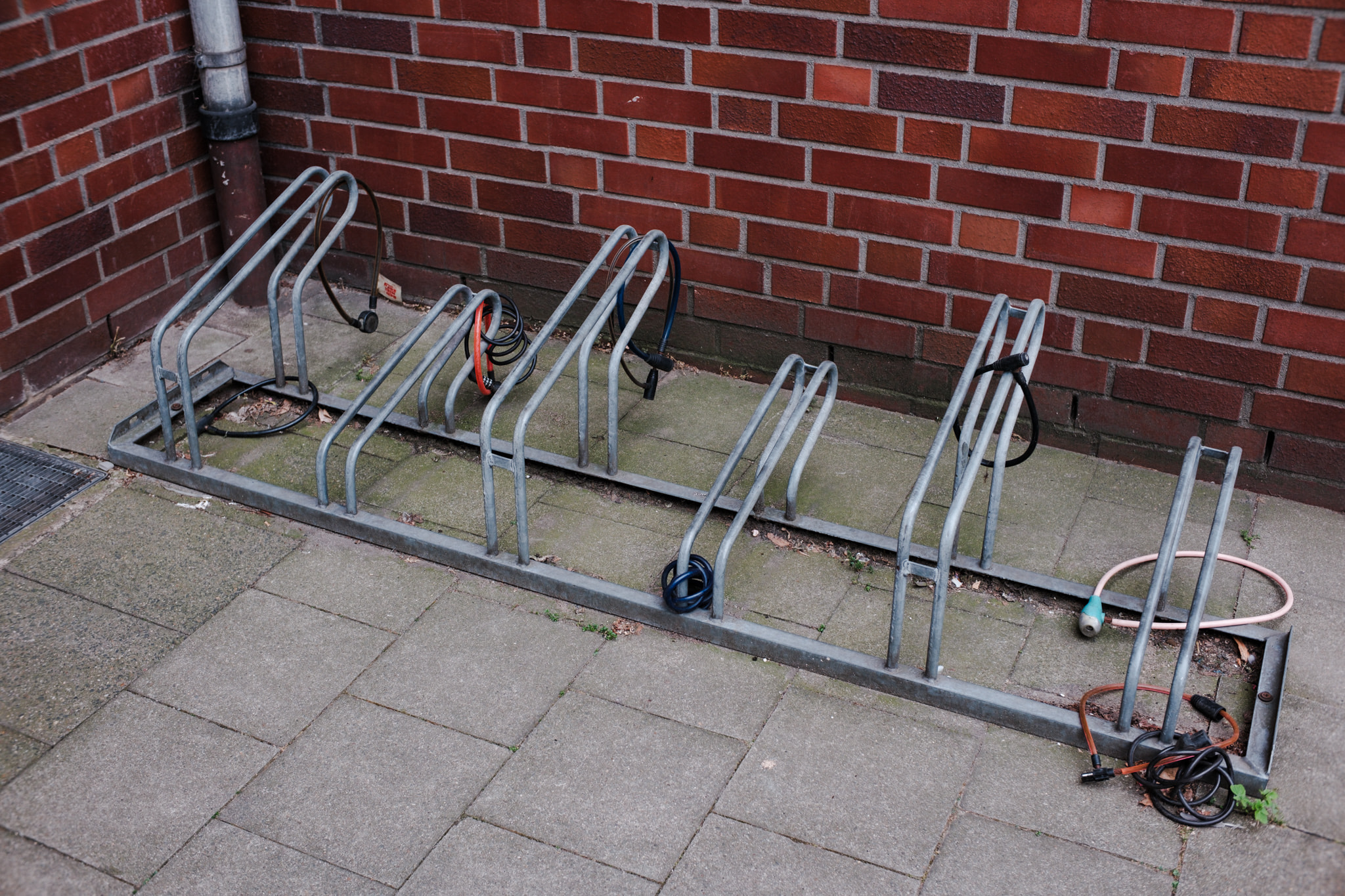 Empty metal bicycle racks against red brick wall on paved ground