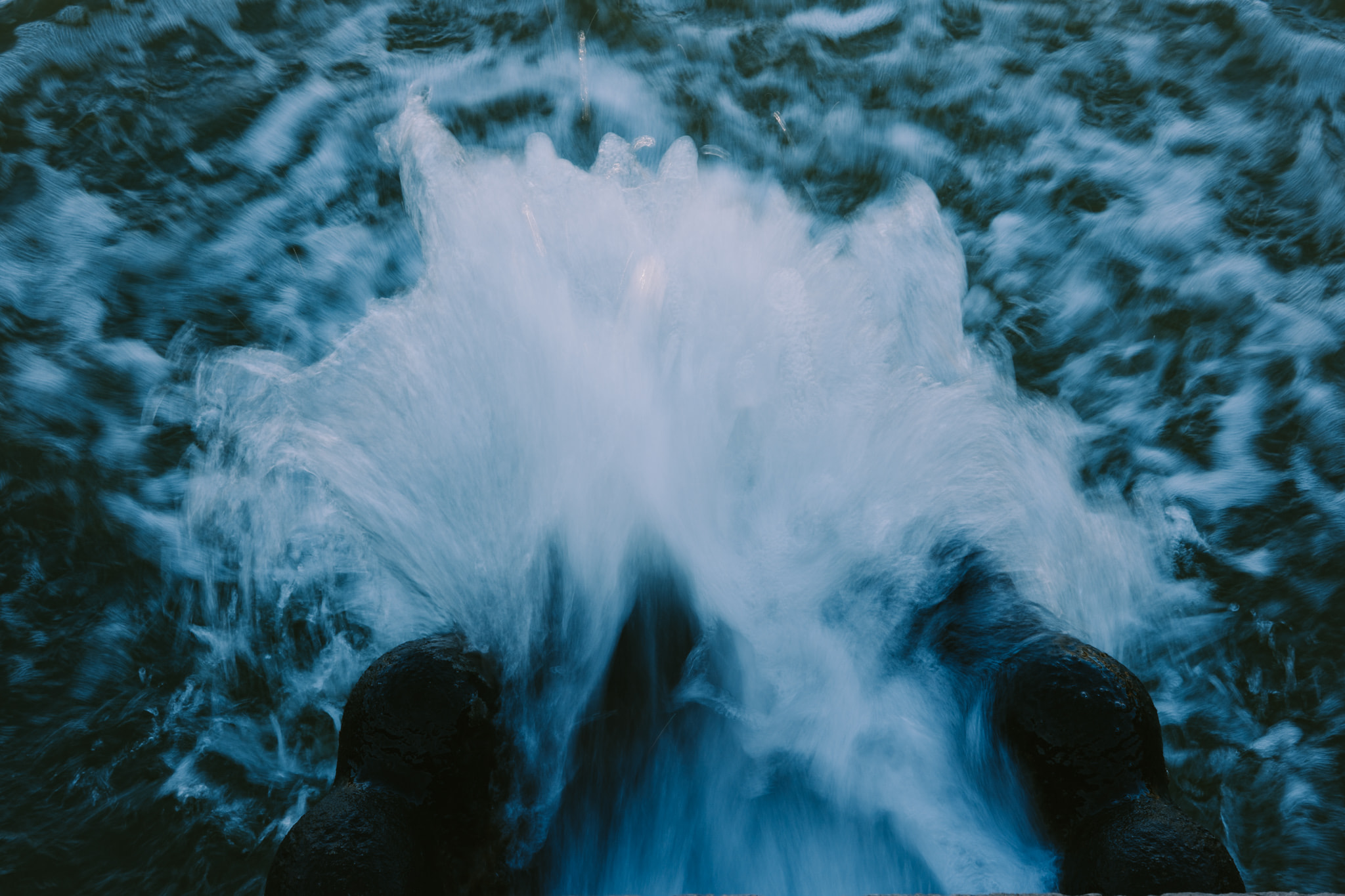 Powerful water rushing from two dark pipes into a pool