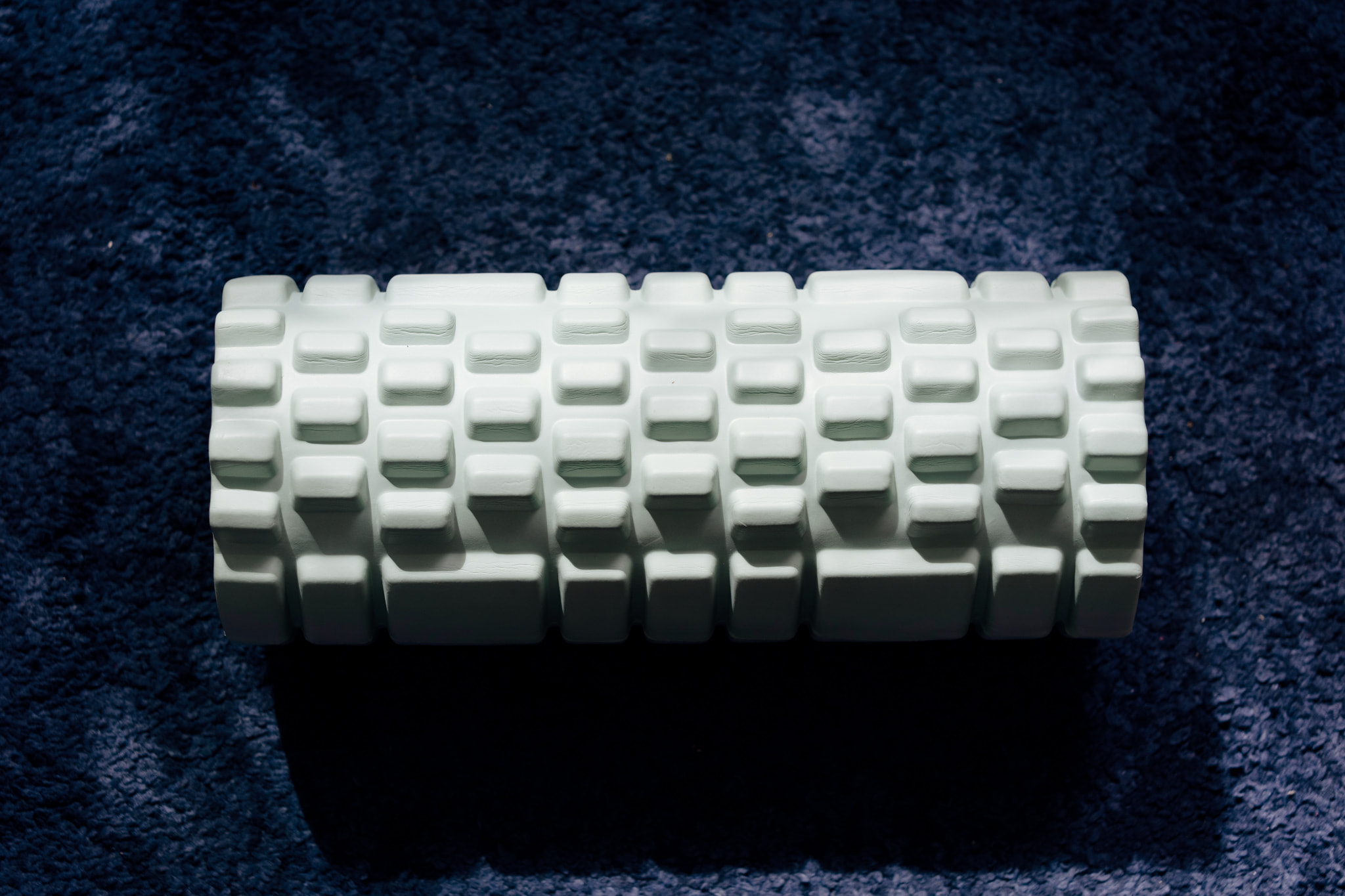 White foam roller with grid pattern on dark blue carpet