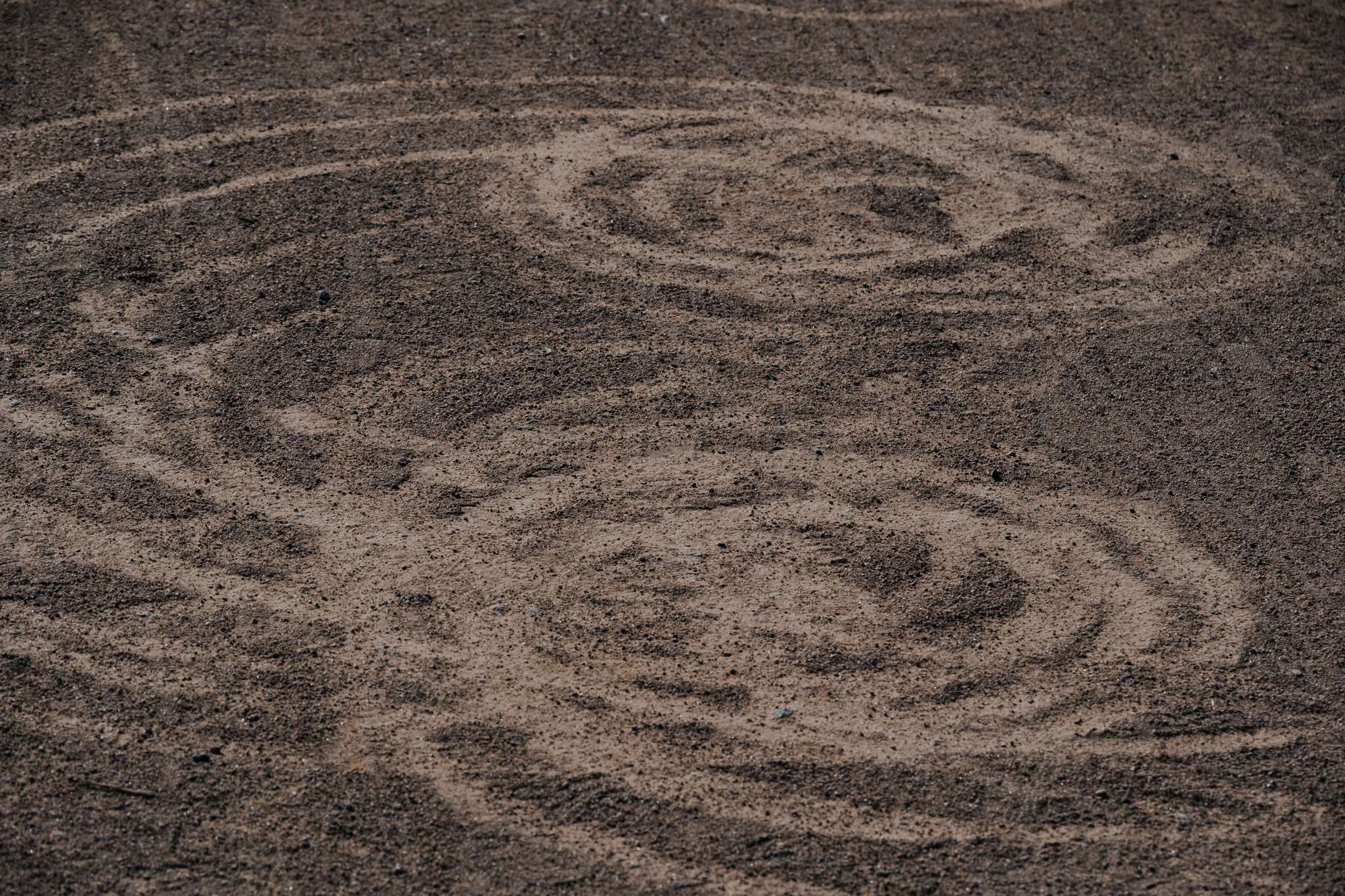 Overlapping circular tire tracks on dark brown dirt ground