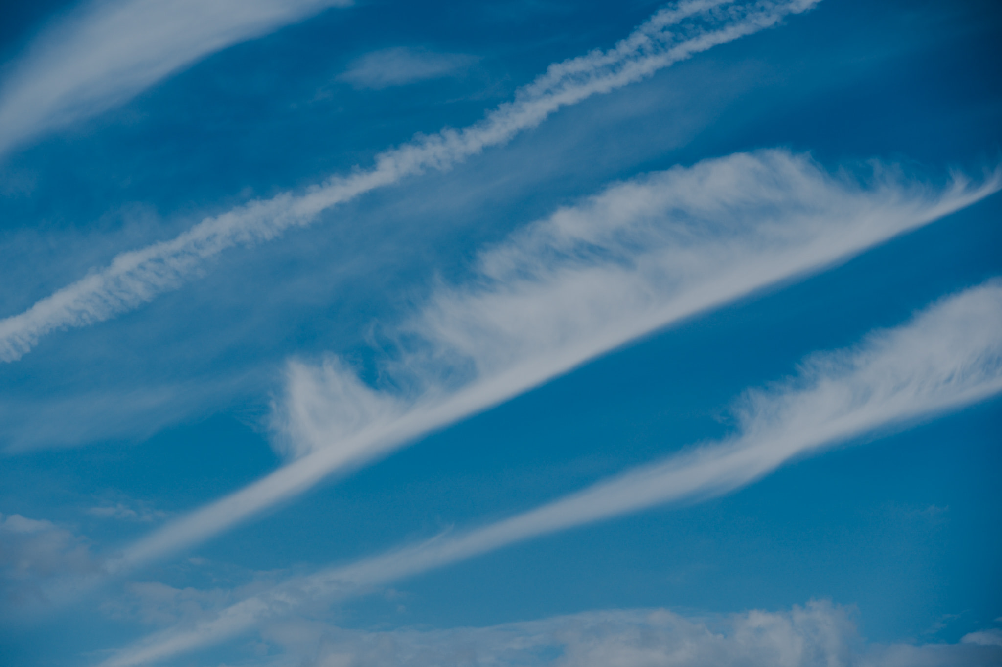 Wispy cirrus clouds and jet contrails streaking diagonally across bright blue sky