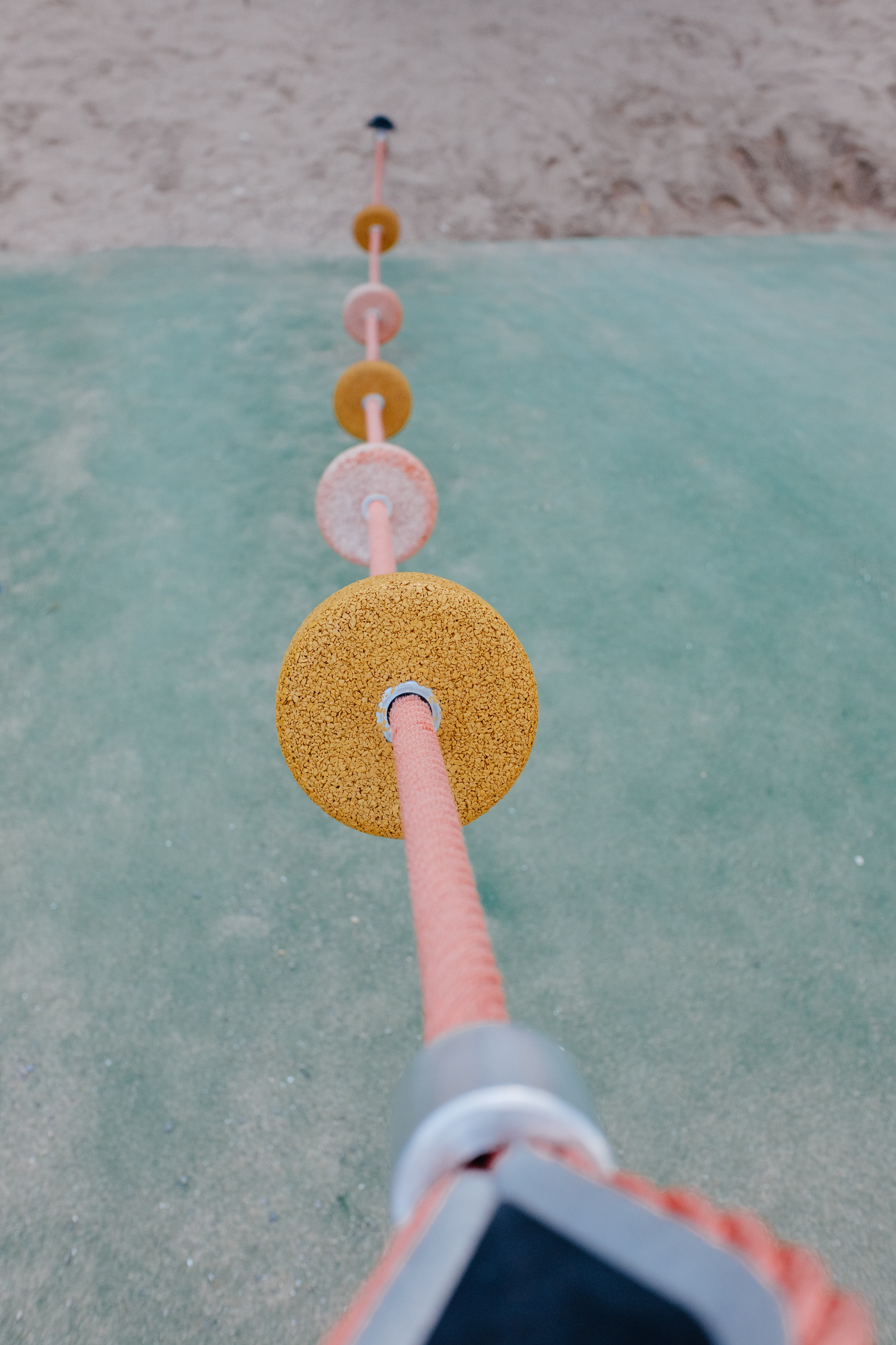 Pink playground climbing rope with round footholds over green safety surface