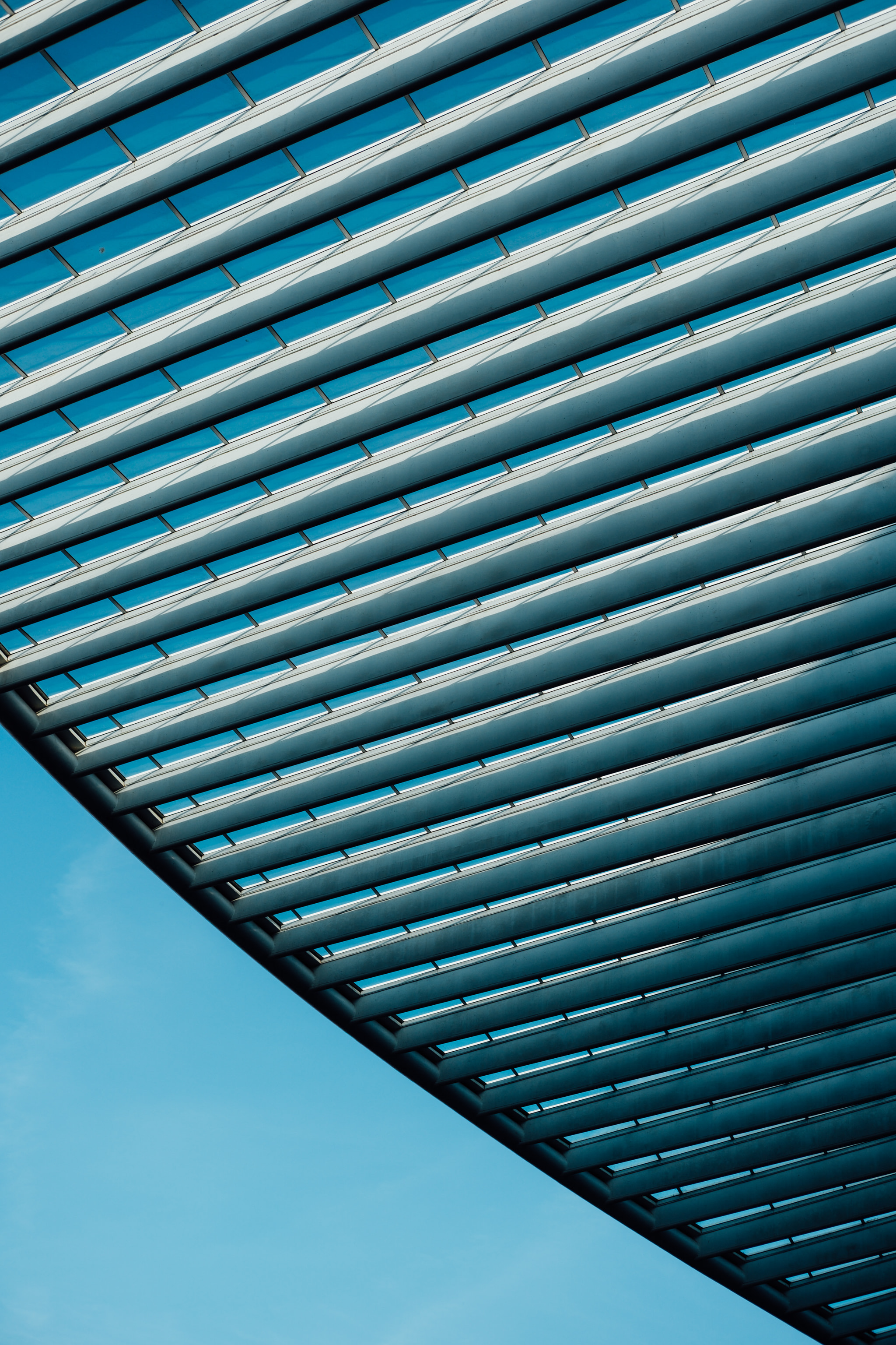 Diagonal steel slat roof canopy against clear blue sky in Liege