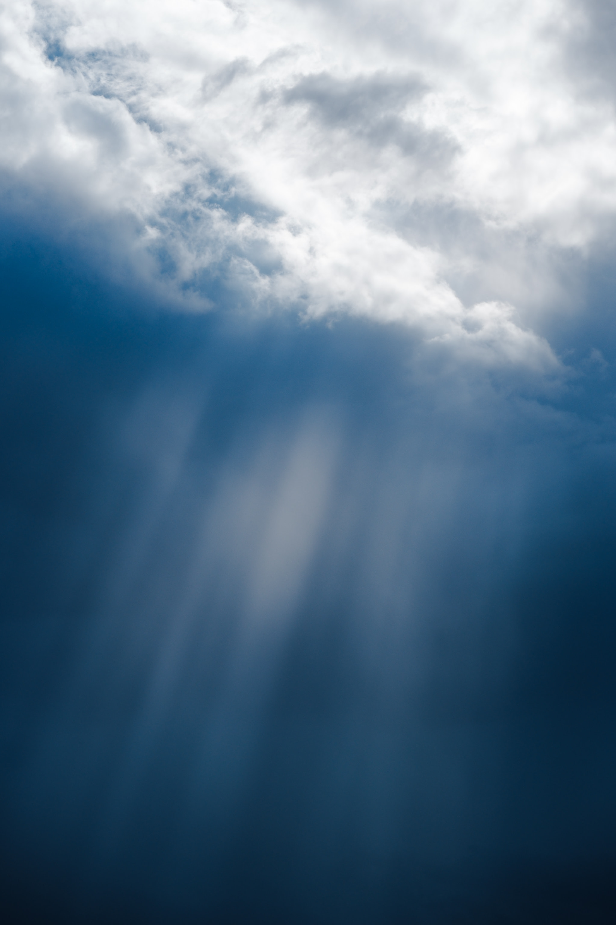 Sunbeams breaking through dramatic clouds in deep blue sky with crepuscular rays