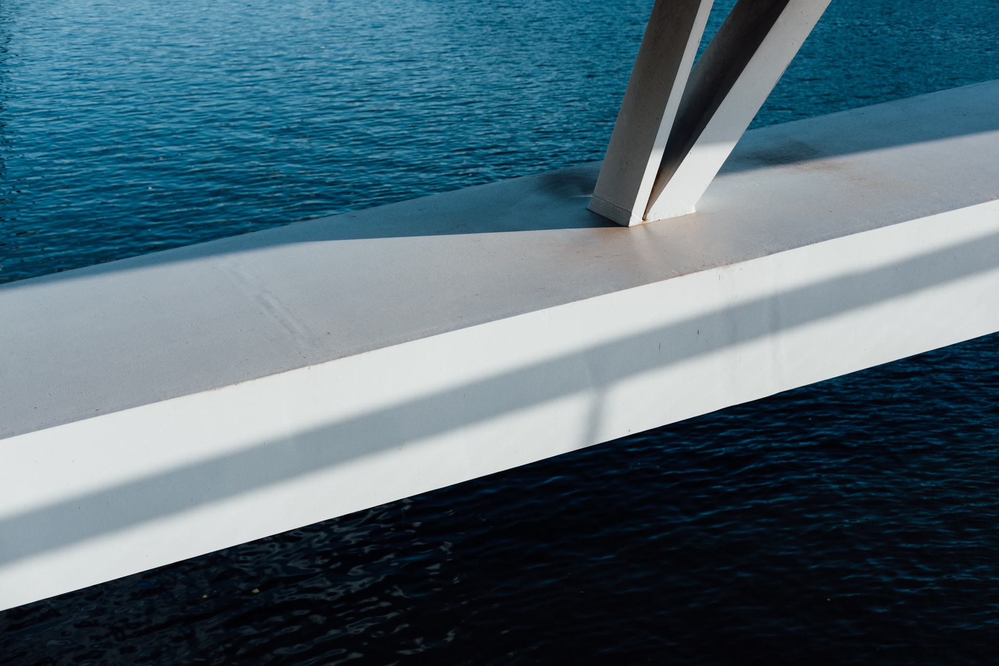 White steel bridge beam over blue water with diagonal shadows