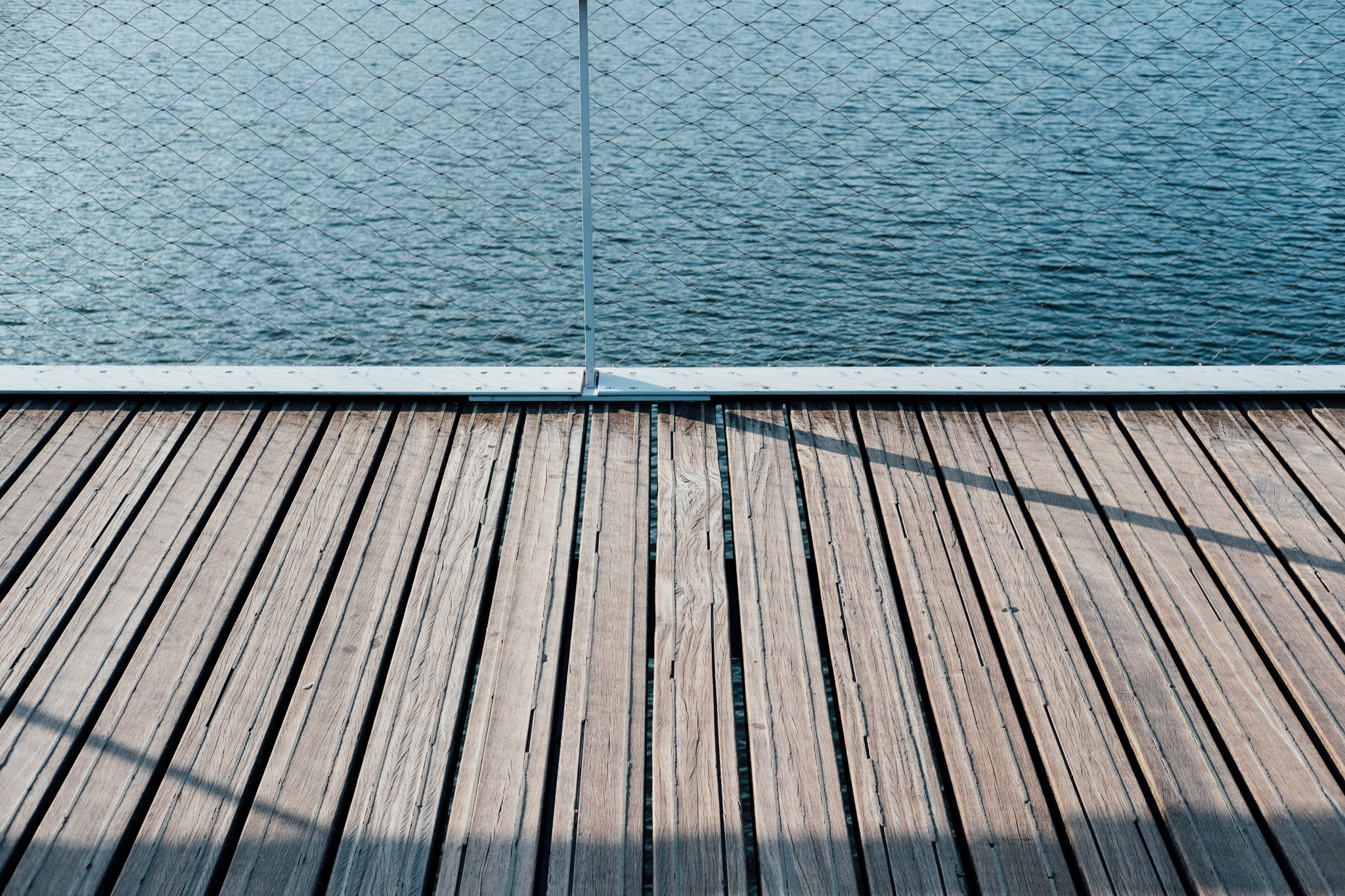 Weathered wooden boardwalk deck with wire fence overlooking calm blue water