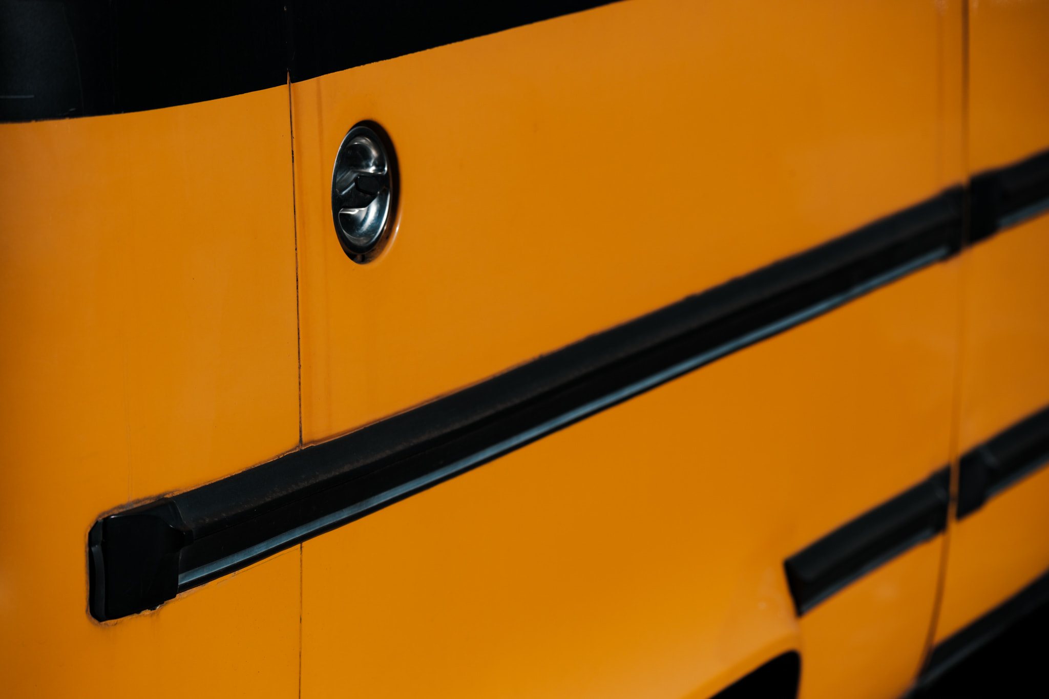 Close-up of yellow school bus side panel with black rub rail and chrome fuel door